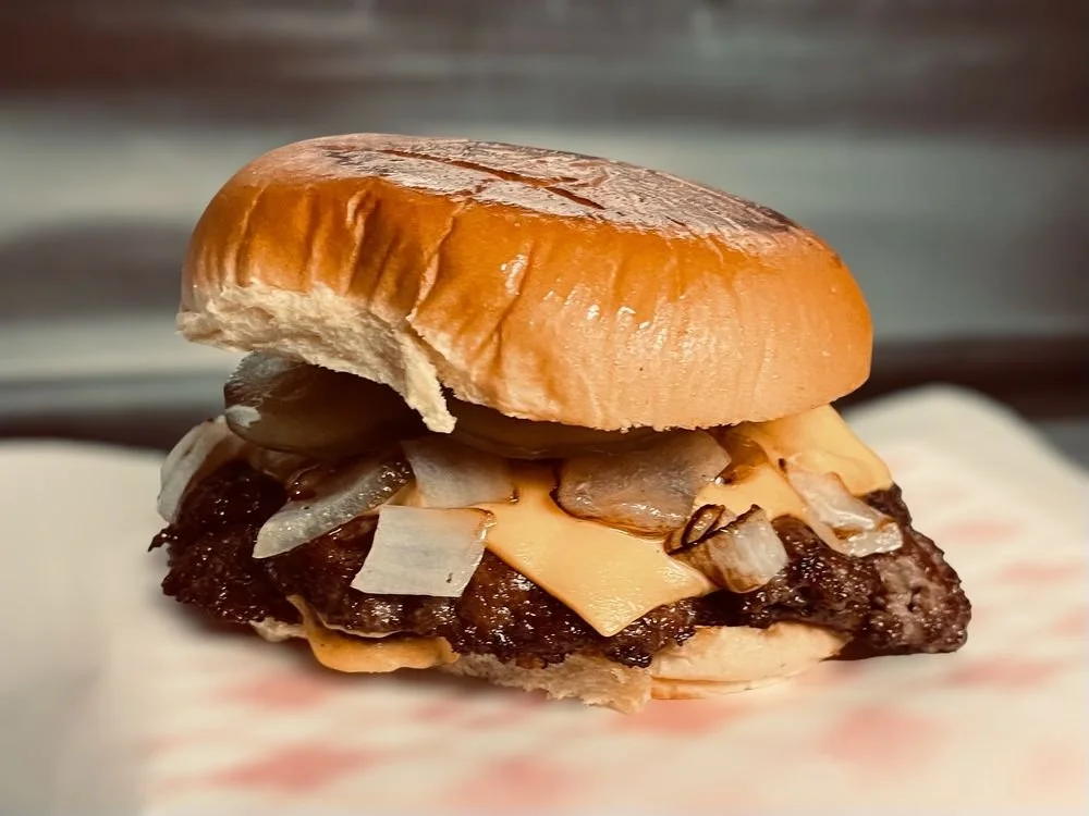 Close-up of a cheeseburger with onion, melted cheese, and a toasted bun.