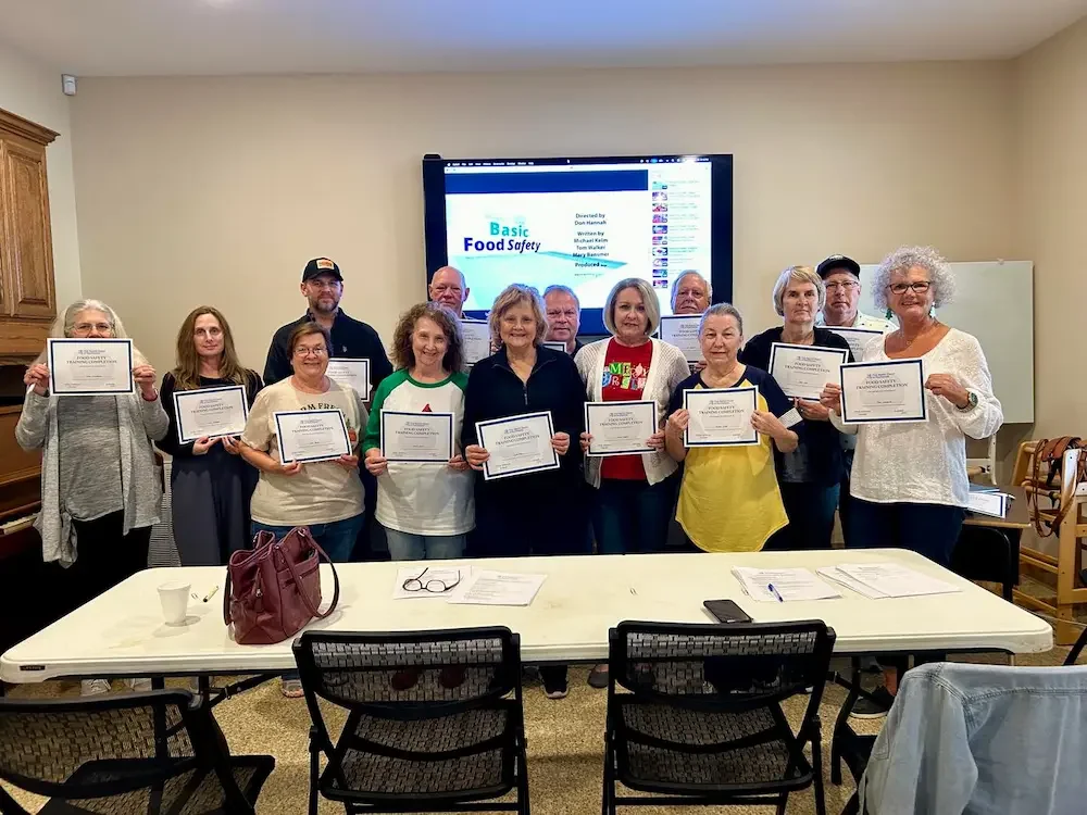 Hospitality ministry kitchen crew volunteers gathered for a group picture, holding up their Food Safety Training certificates