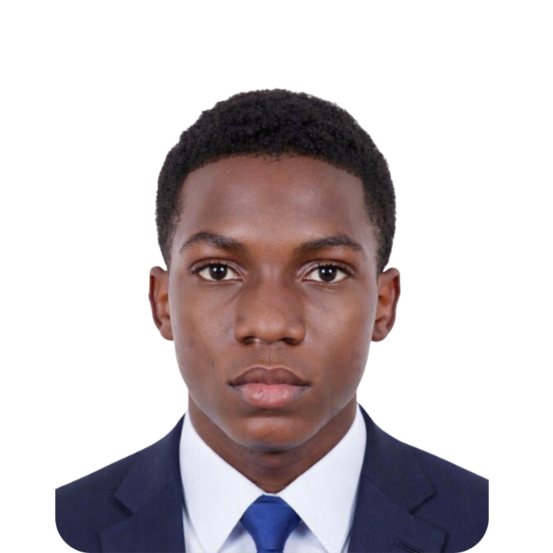 A young man with dark skin, short curly black hair, wearing a navy blue suit, white shirt, and blue tie, looking directly at the camera against a plain white background.