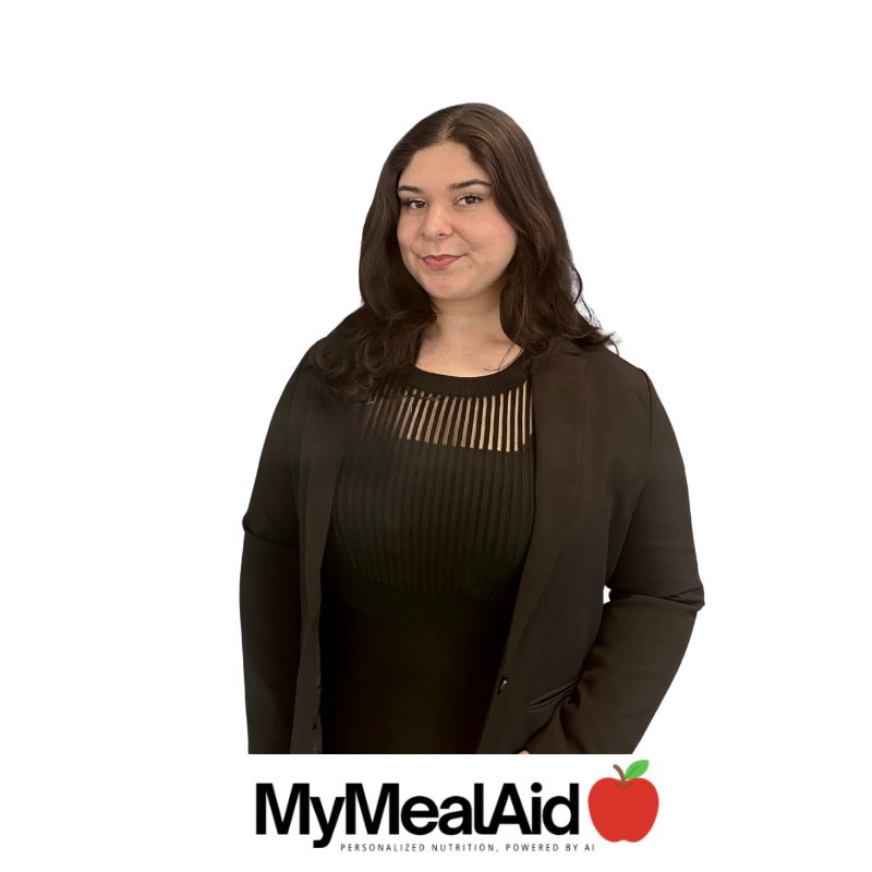 A woman with shoulder-length dark hair wearing a black top and black blazer standing against a white background, with the MyMealAid logo and an apple graphic at the bottom.