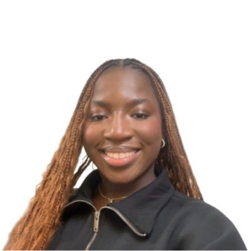 Portrait of a smiling woman with long, braided hair, wearing a black zip-up jacket and hoop earrings, against a plain white background.