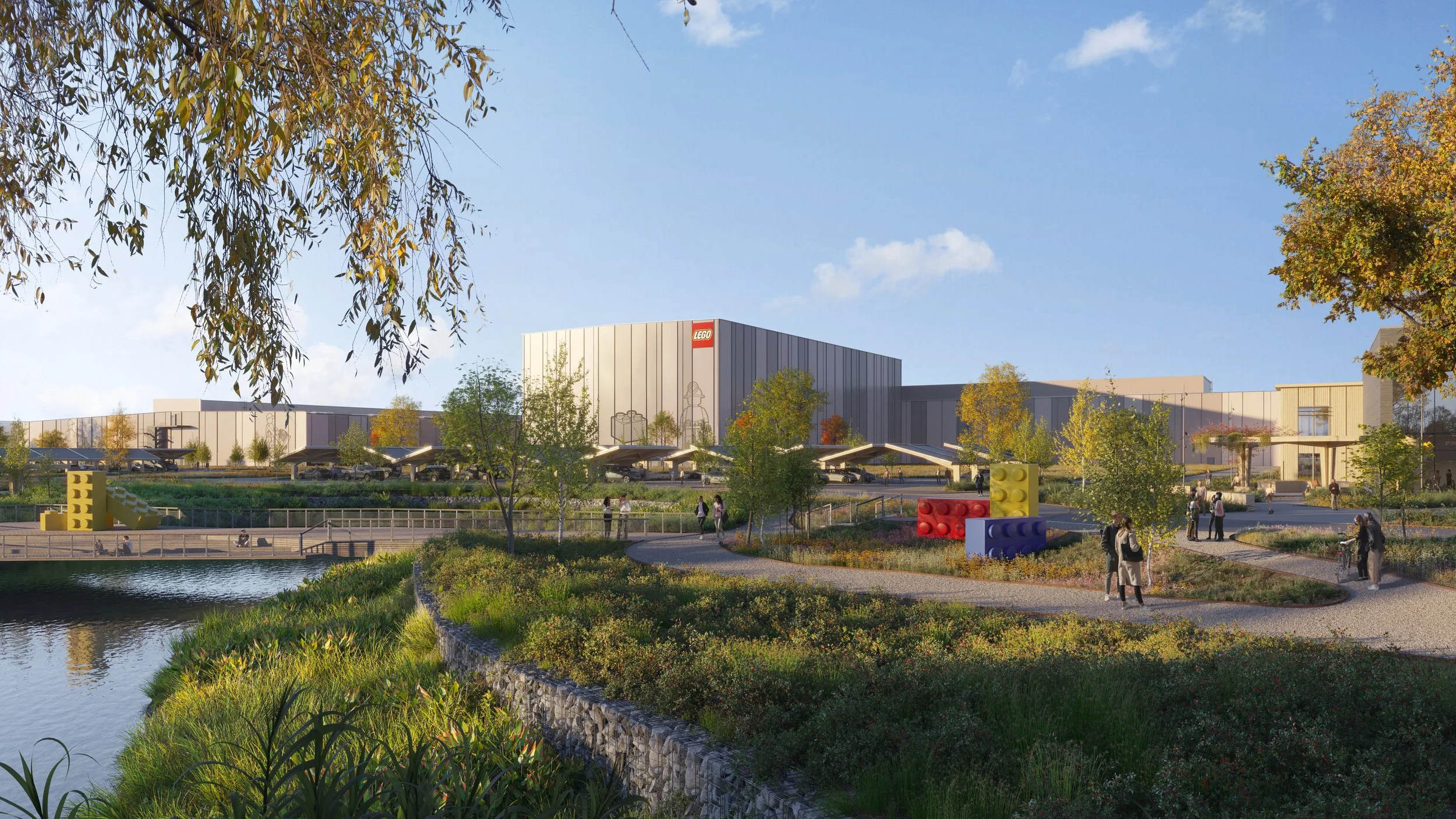 A modern LEGO retail store with a parking lot, surrounded by trees and a small water body, during daytime with a clear blue sky.