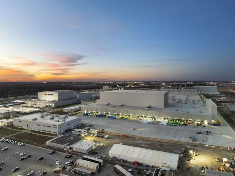 An aerial view of a large industrial warehouse with a parking lot, at sunset with a colorful sky.