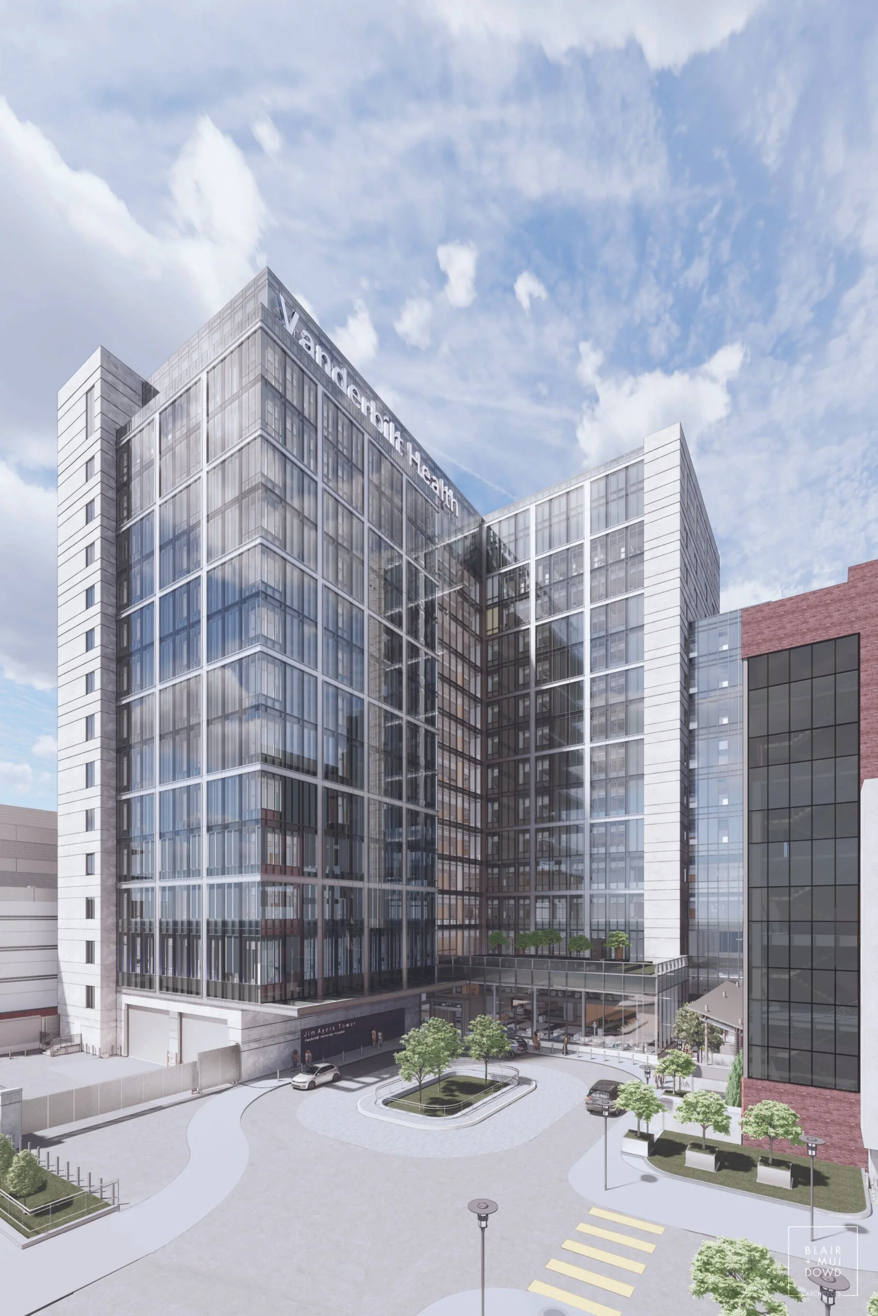 A modern glass office building with a sign that reads 'Vanguard Health' at the top, surrounded by a paved plaza, trees, street lamps, parked cars, and a crosswalk under a partly cloudy sky.