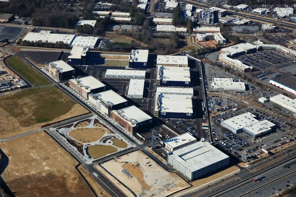 An aerial view of a large modern office complex with parking lots, surrounding roads, and open land areas, some with minimal landscaping.