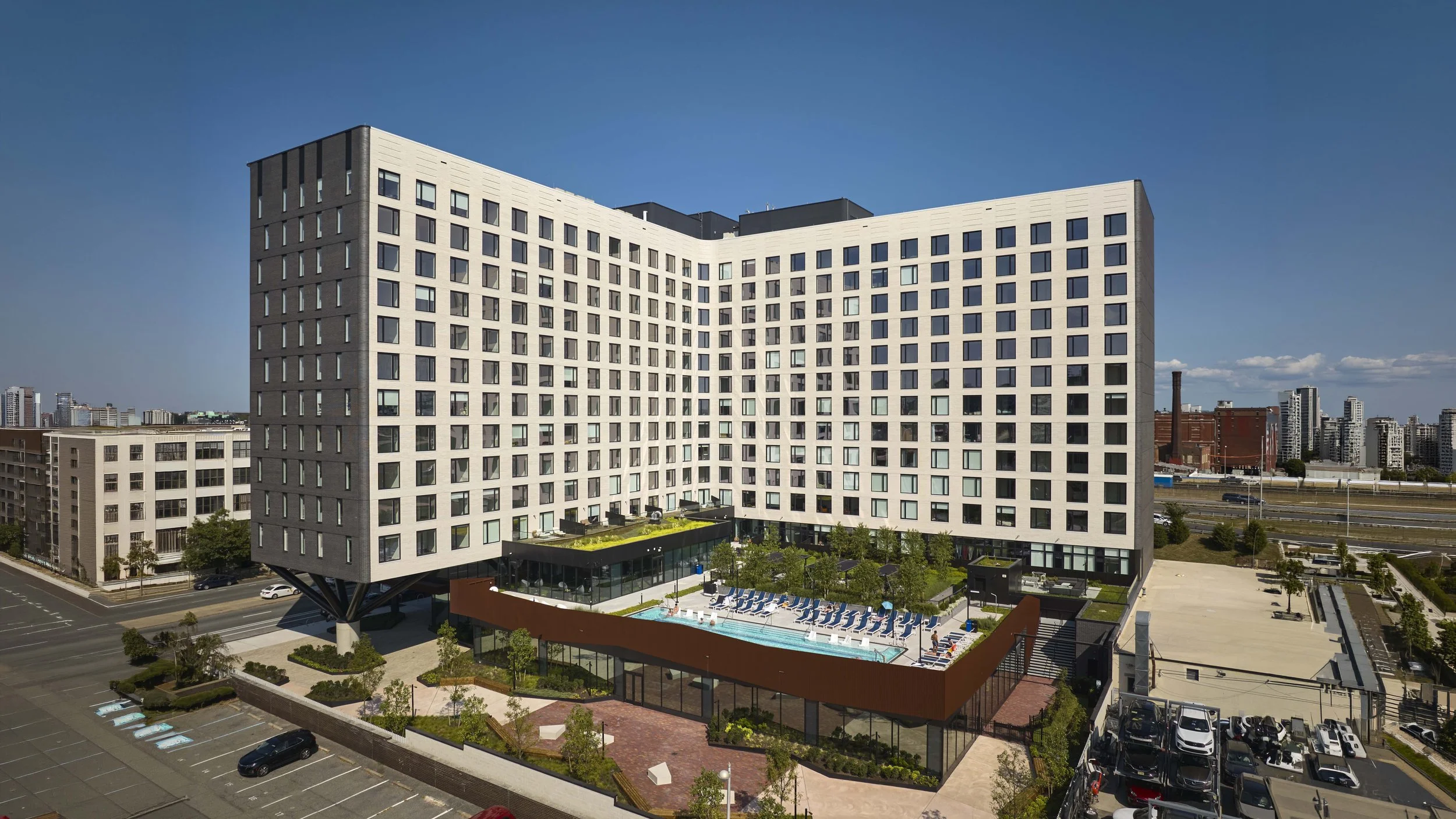 Modern multi-story residential building with a rooftop pool and lounge area, set in an urban environment.