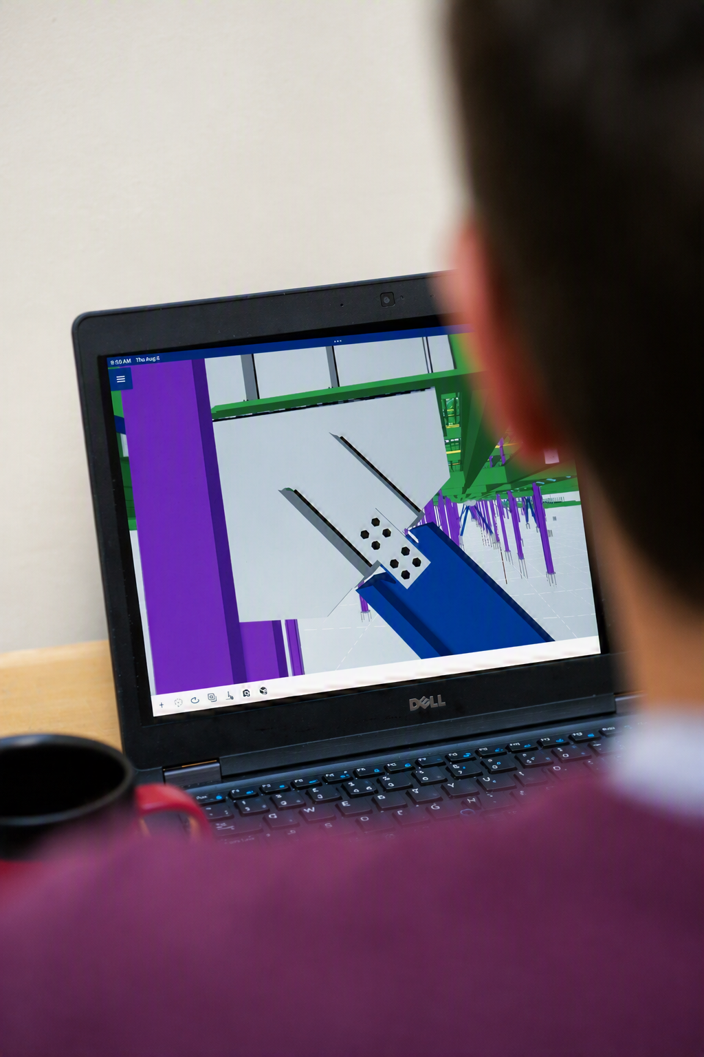 A person looking at a computer monitor displaying a 3D model or virtual environment with colorful graphical elements, including purple, green, and blue structures.