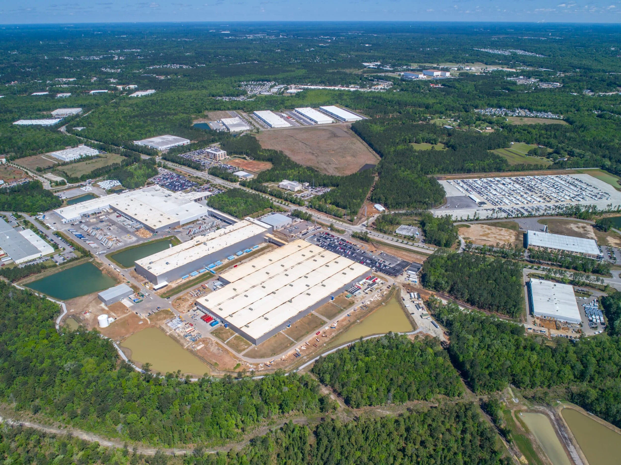 Aerial view of a large industrial or commercial complex surrounded by greenery and trees, with multiple warehouses and parking lots.