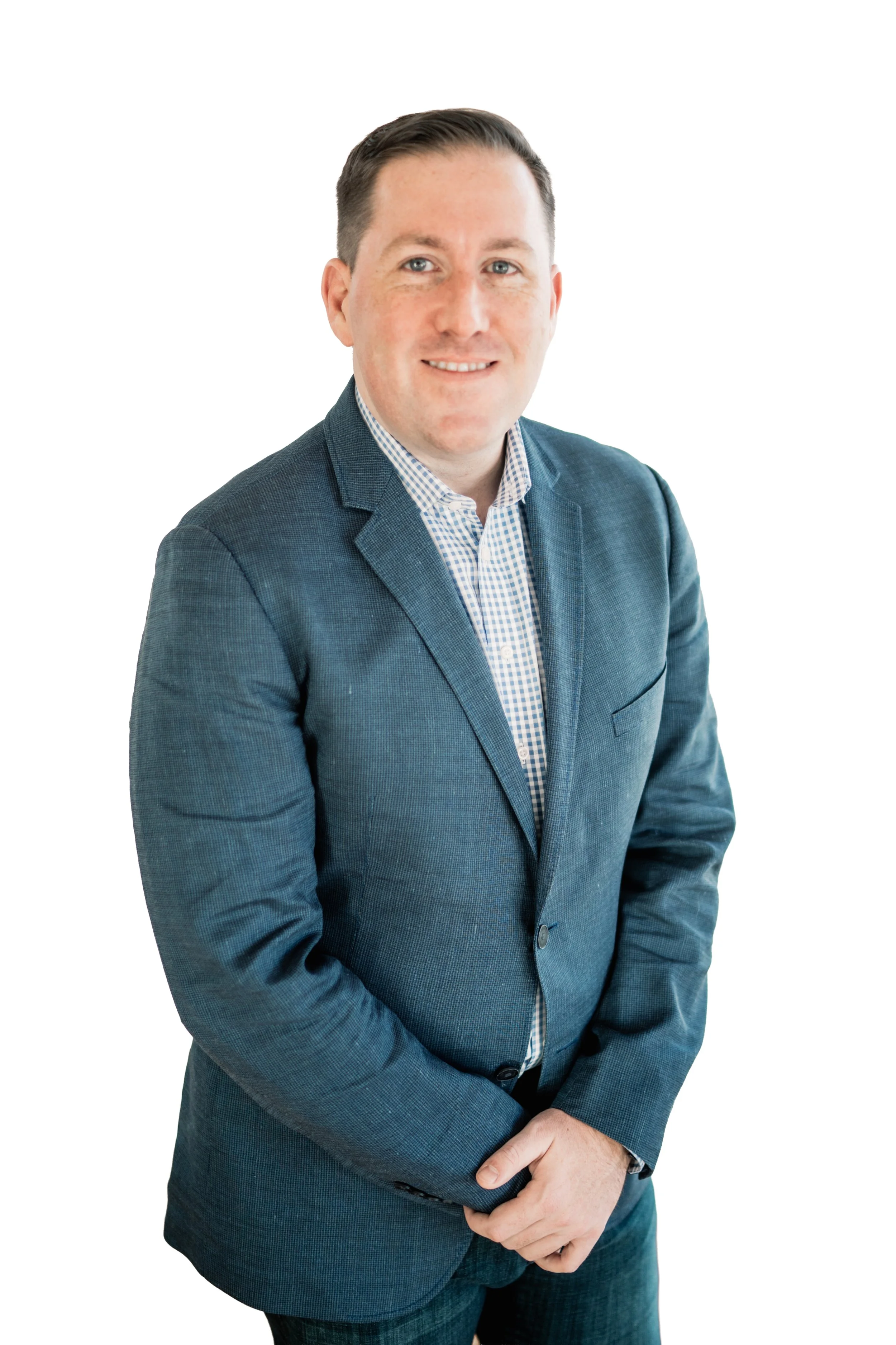 A man with short dark hair wearing a blue checked blazer and a dress shirt posing against a plain white background.
