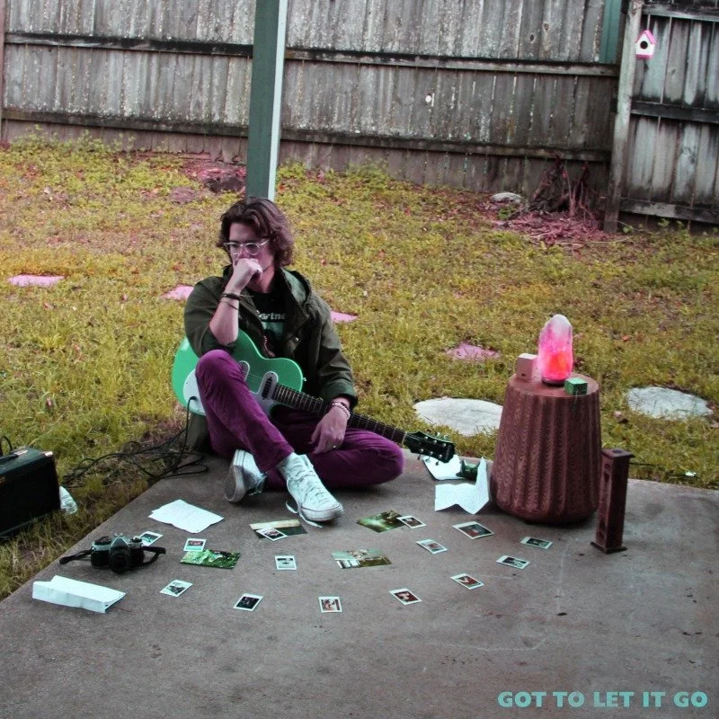 William Creamer sitting on a patio with a turquoise guitar, surrounded by photographs and mementos, with a backyard and wooden fence in the background. The text overlay says "Got to Let it Go".