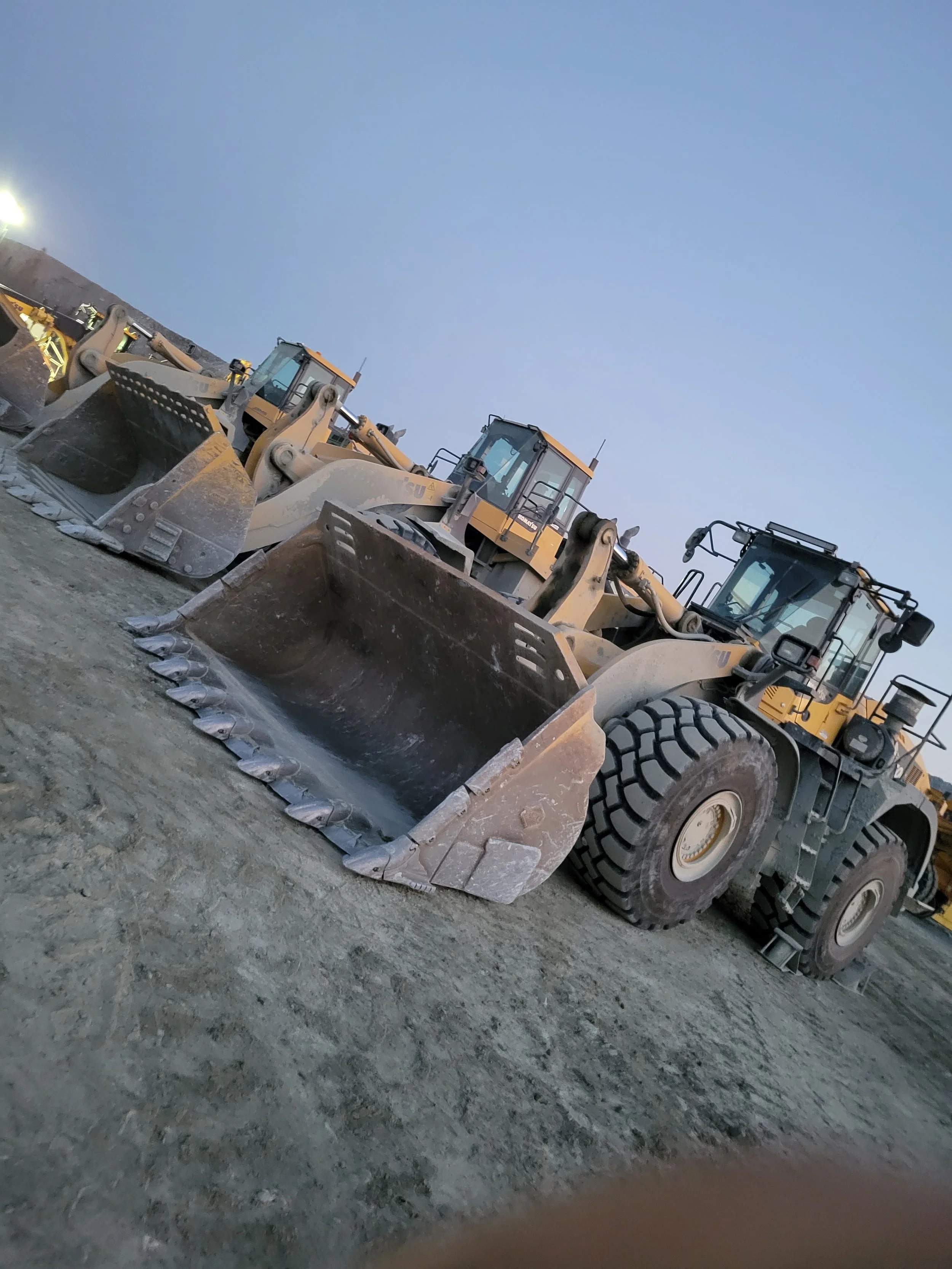 Several large construction bulldozers parked on a dirt lot during dusk or early evening.