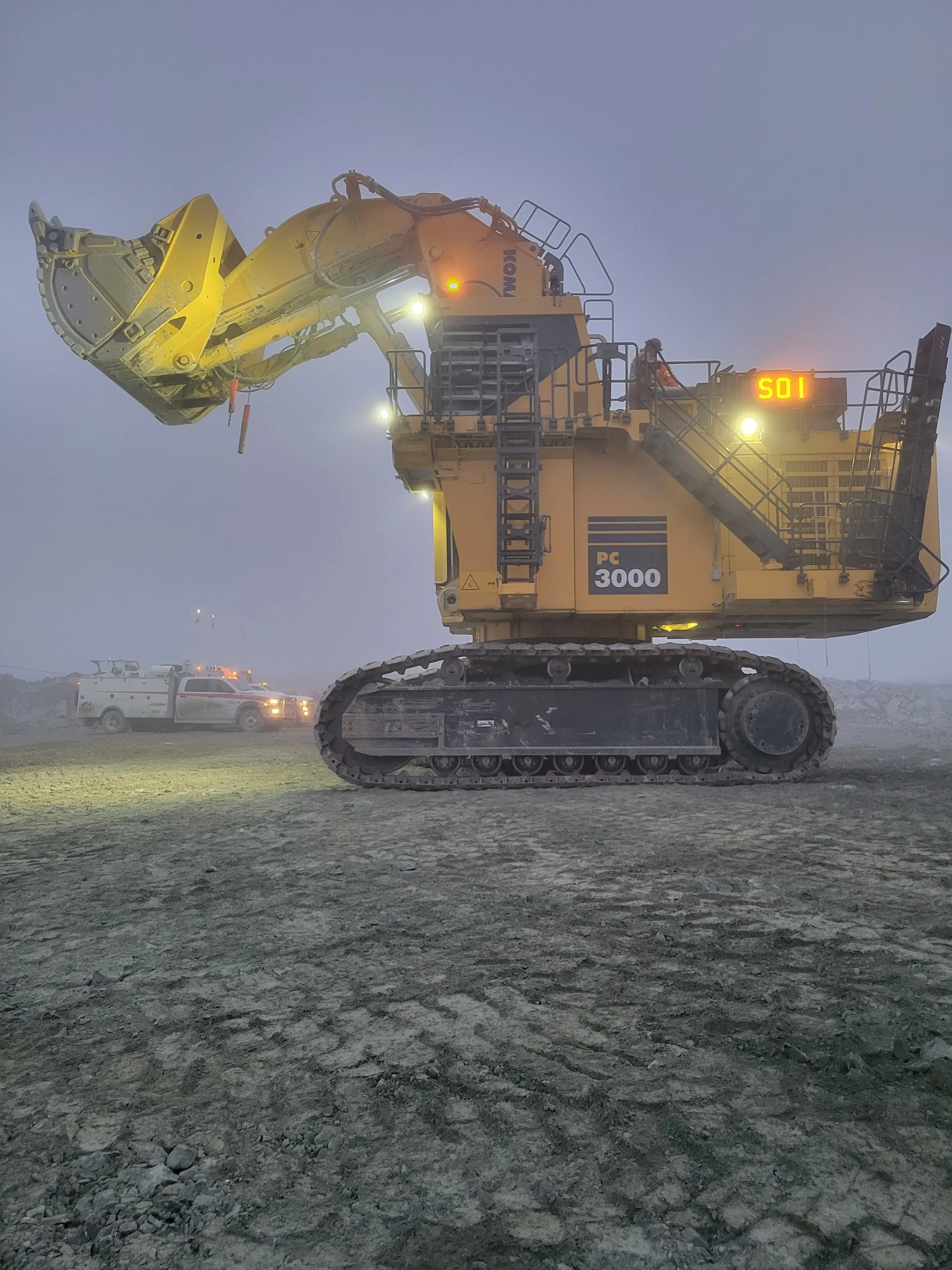Heavy construction excavator at a construction site during foggy weather with a police or emergency vehicle nearby.