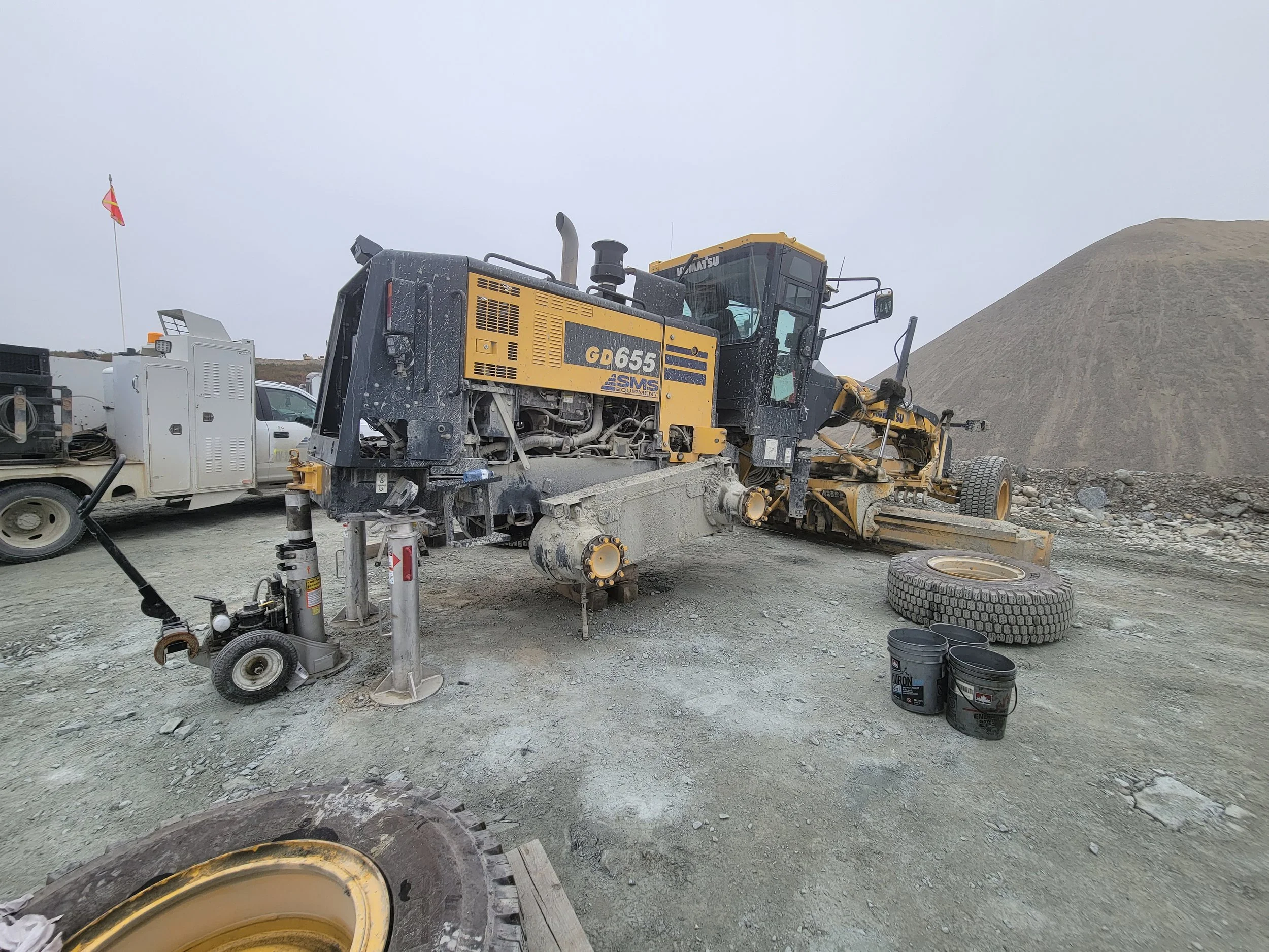 Construction site with a large yellow road roller and other construction vehicles, a pile of dirt in the background, and buckets on the ground.