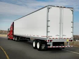 A large white semi-truck trailer on a road, attached to a red cab.