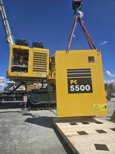 Yellow industrial equipment labeled 'PC 5500' being lowered onto a wooden platform at a construction site.