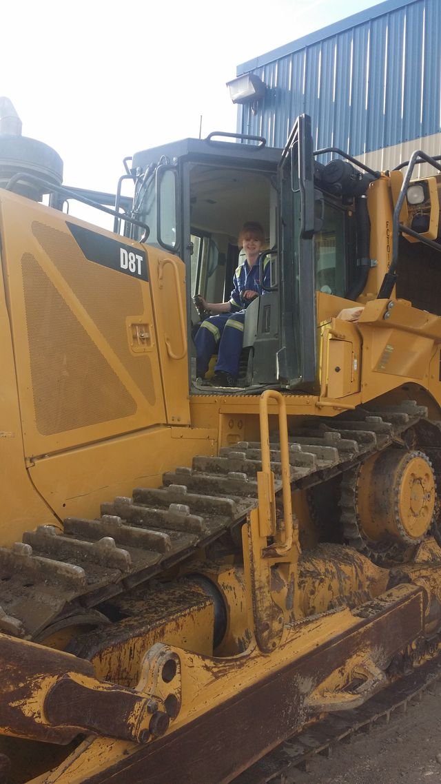 Child sitting inside the cab of a large yellow bulldozer at a construction site.