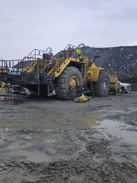Large yellow mining dump truck at a mining site with dirt and gravel terrain and overcast sky.