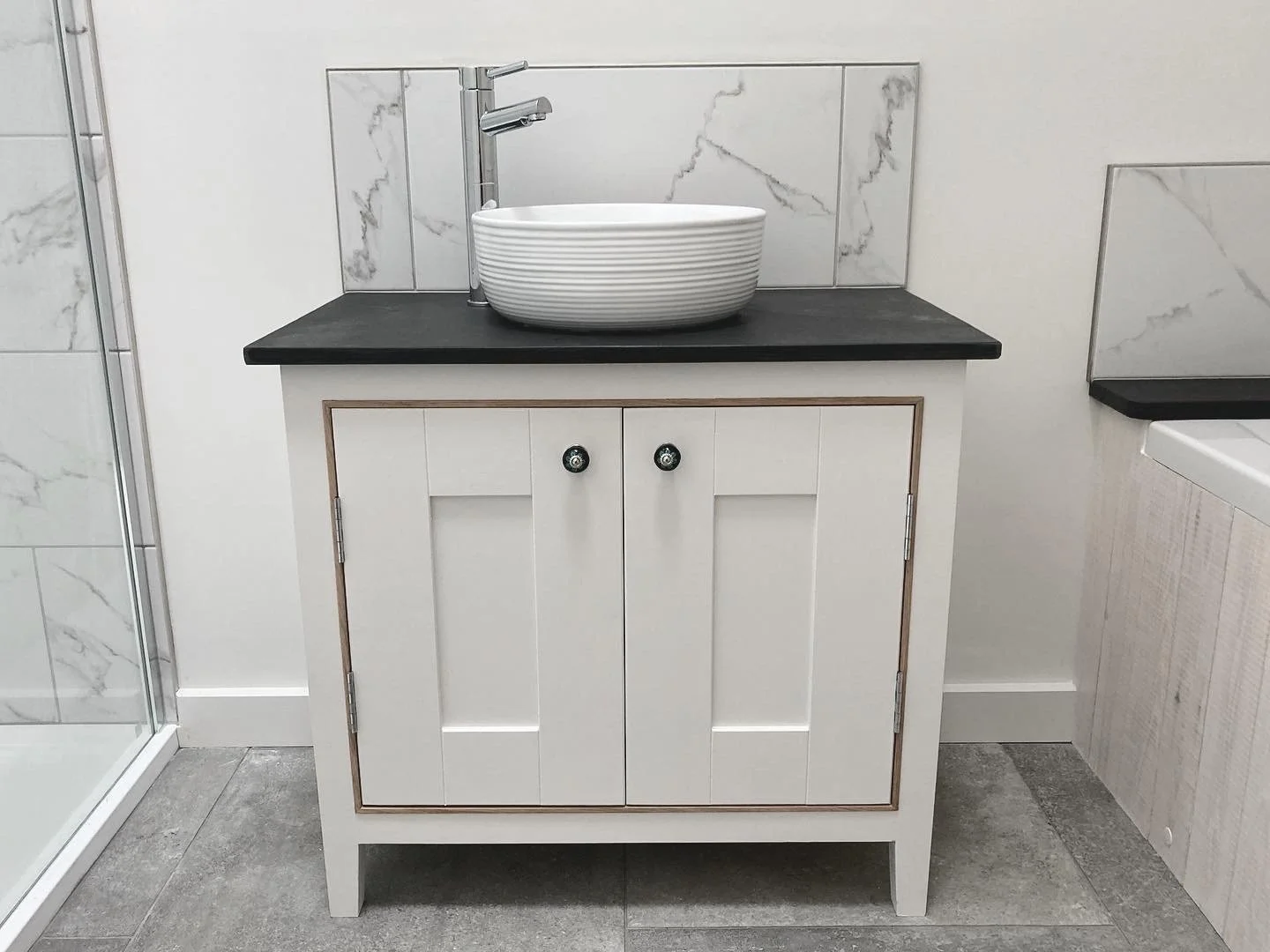 White bathroom handmade vanity with black countertop, vessel sink, chrome faucet, and marble-look tile backsplash