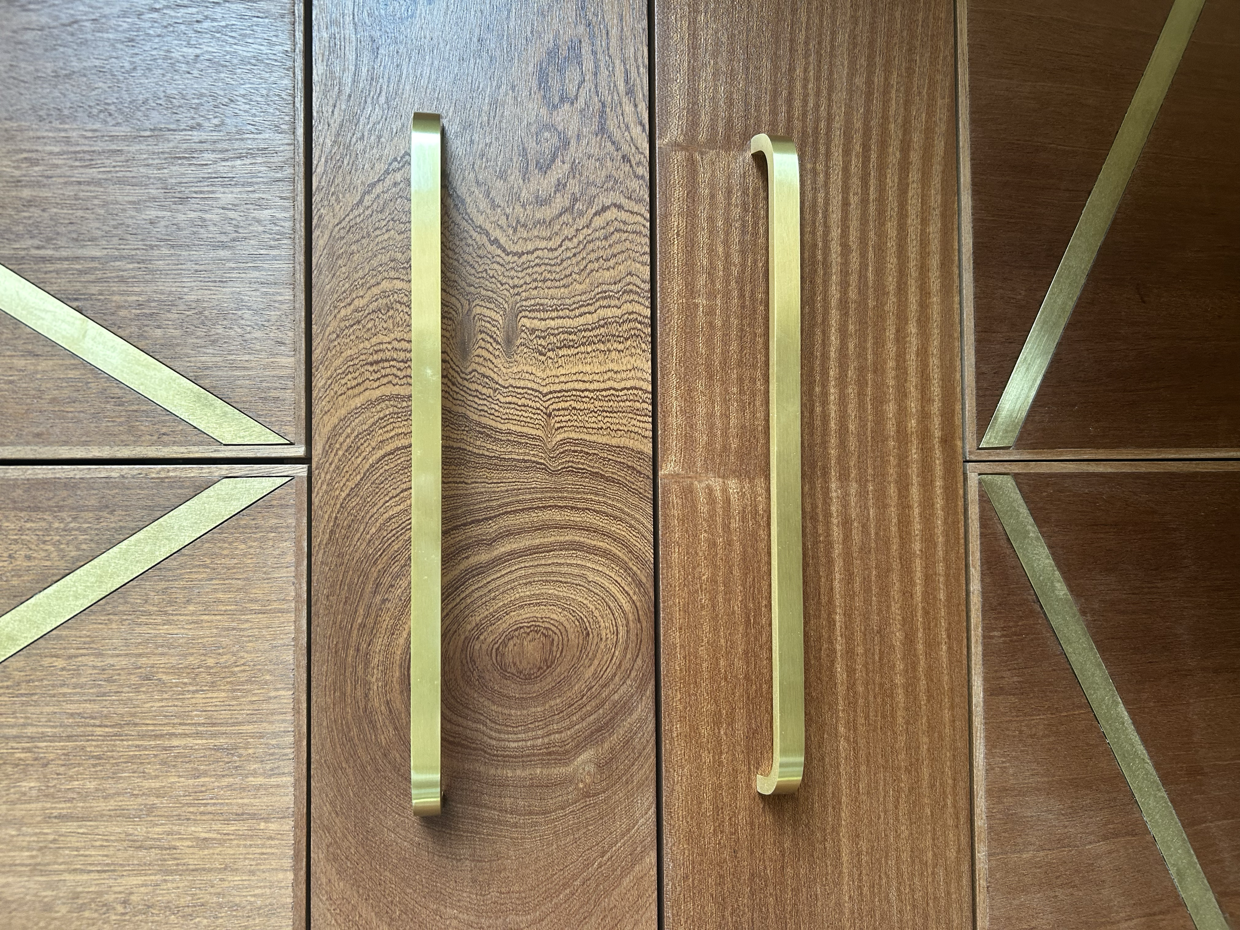 Brushed brass cabinet handles and decorative inlay strips displayed on a dark wood cabinet.