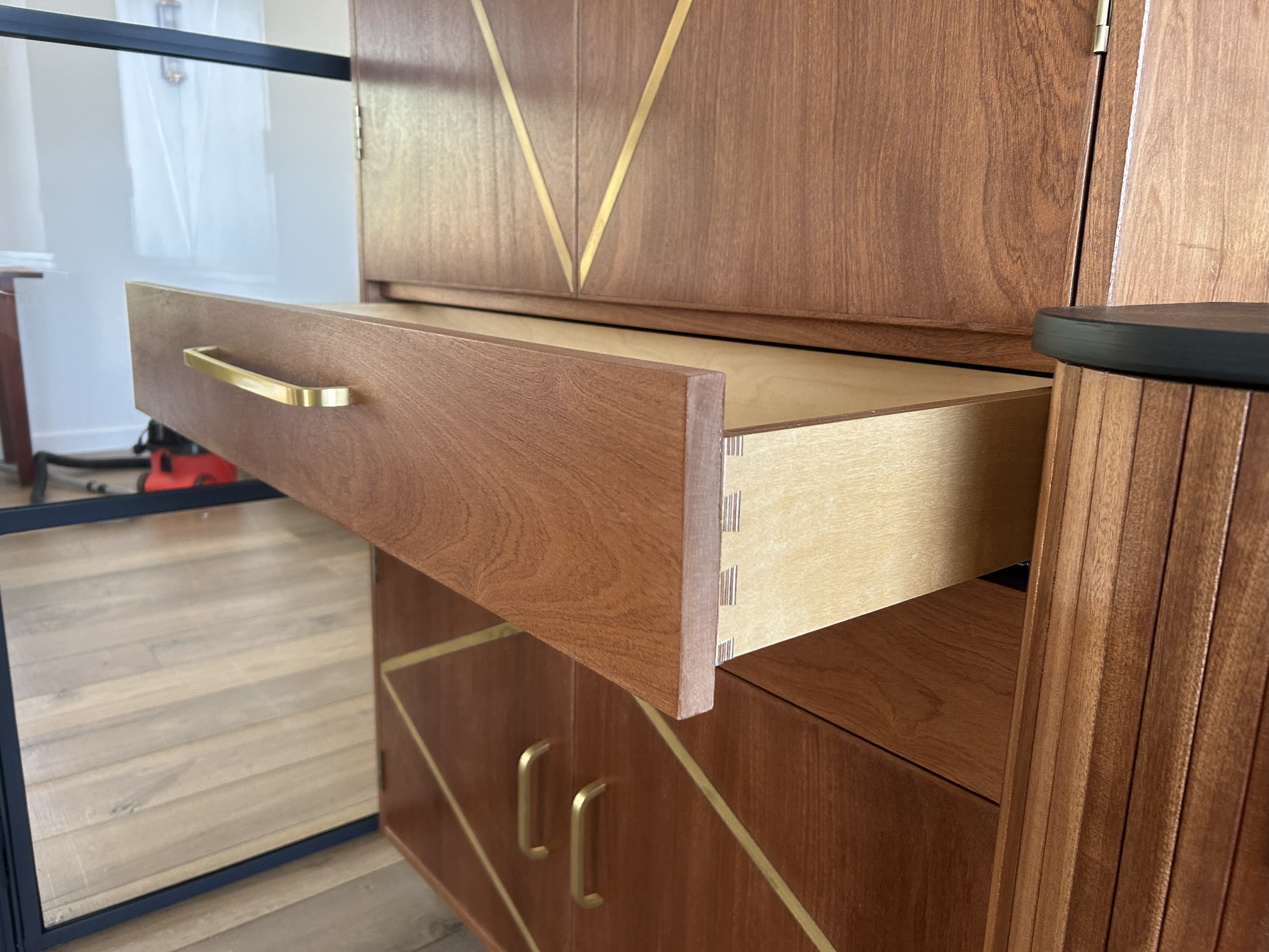 Close-up of a mid-century hand made wooden cabinet with open drawers, brass handles, and geometric gold trim.