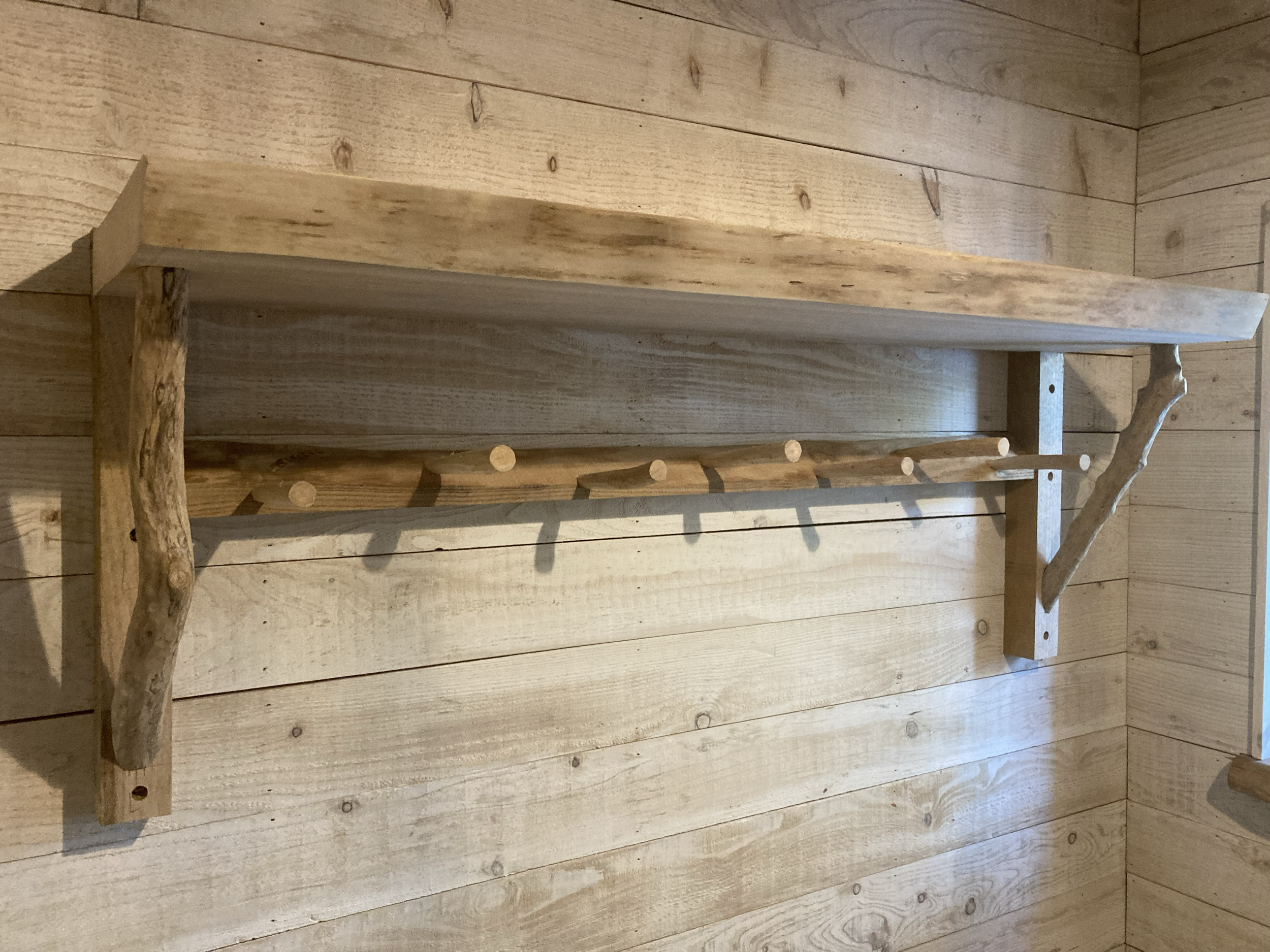 Rustic wooden wall-mounted shelf with natural branch supports in a wood-paneled room