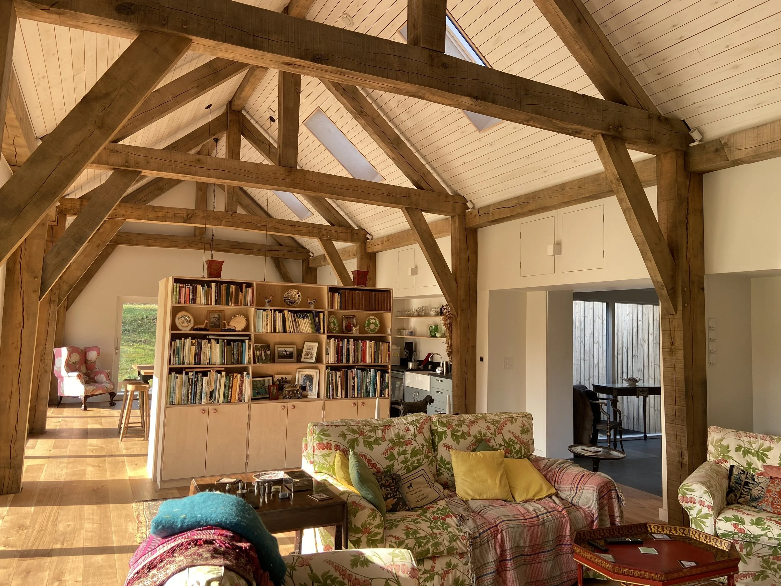 Bright rustic living room with exposed timber beams, a large built-in bookshelf and vaulted wood-paneled ceiling.
