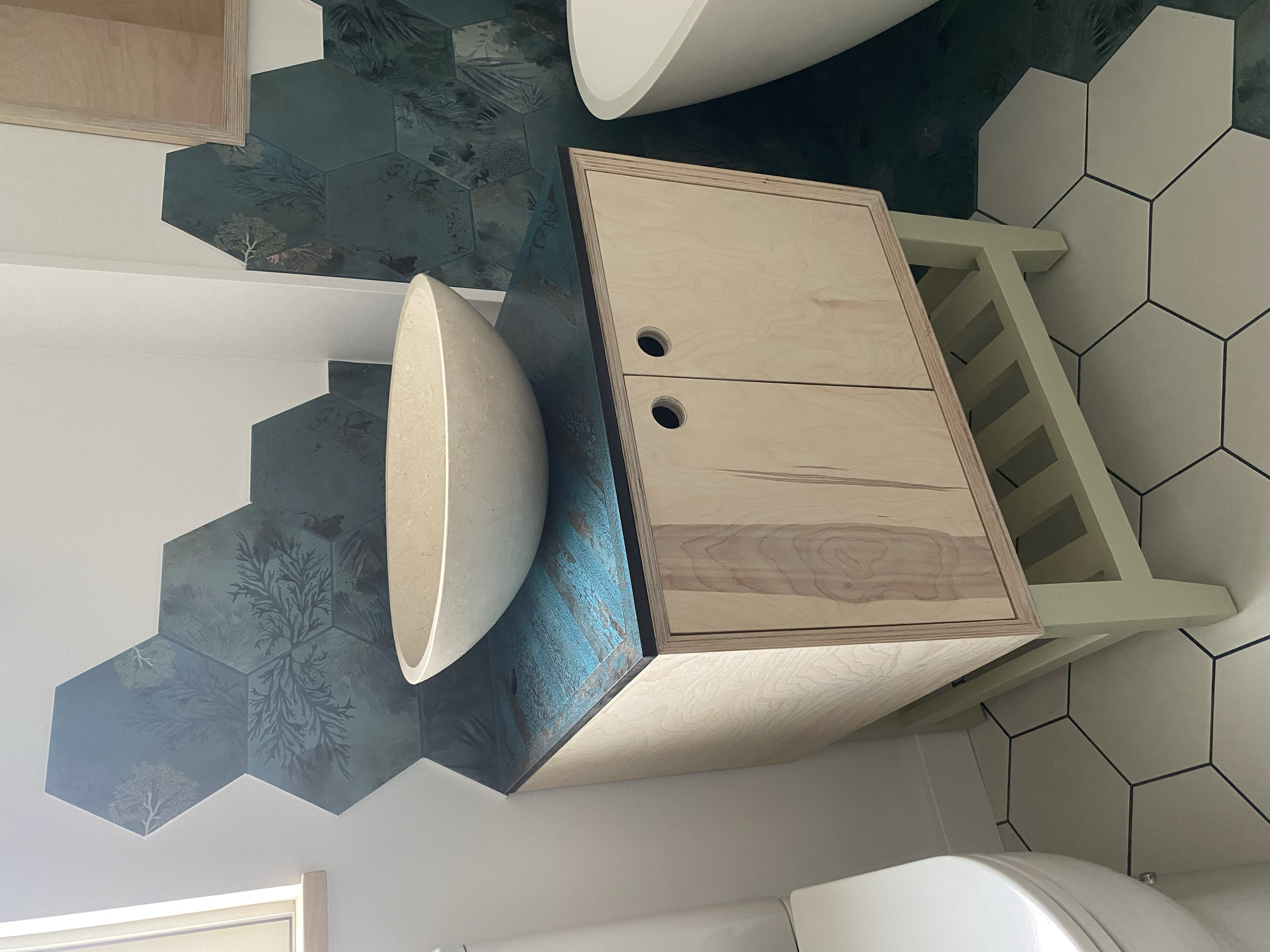 Modern bathroom with a white vessel sink on a light hand made birch ply wood vanity, teal botanical hexagon backsplash, and hexagonal floor tiles