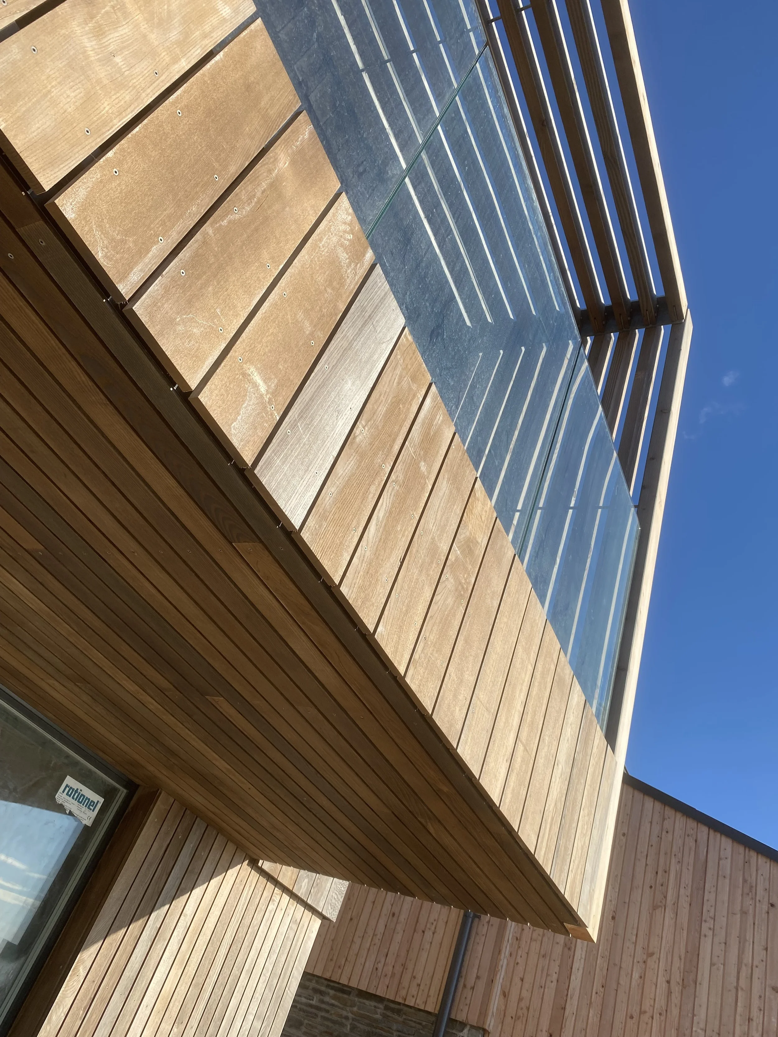 Modern building exterior with wood paneling and glass balcony railings, under a clear blue sky.