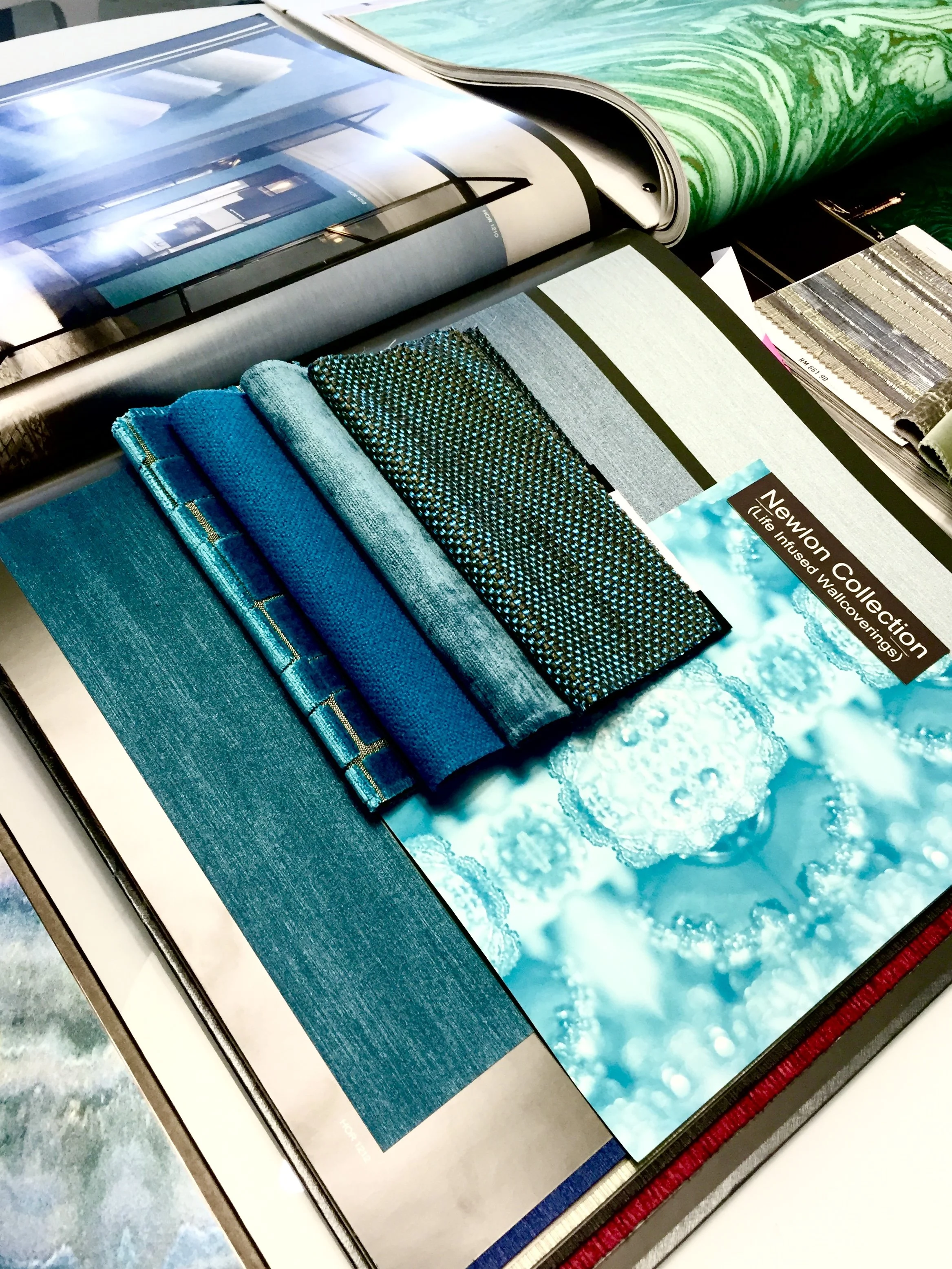 A collection of fabric swatches in various shades of blue and green, along with a brochure from the Newwin Collection displaying a blue water and sky scene.