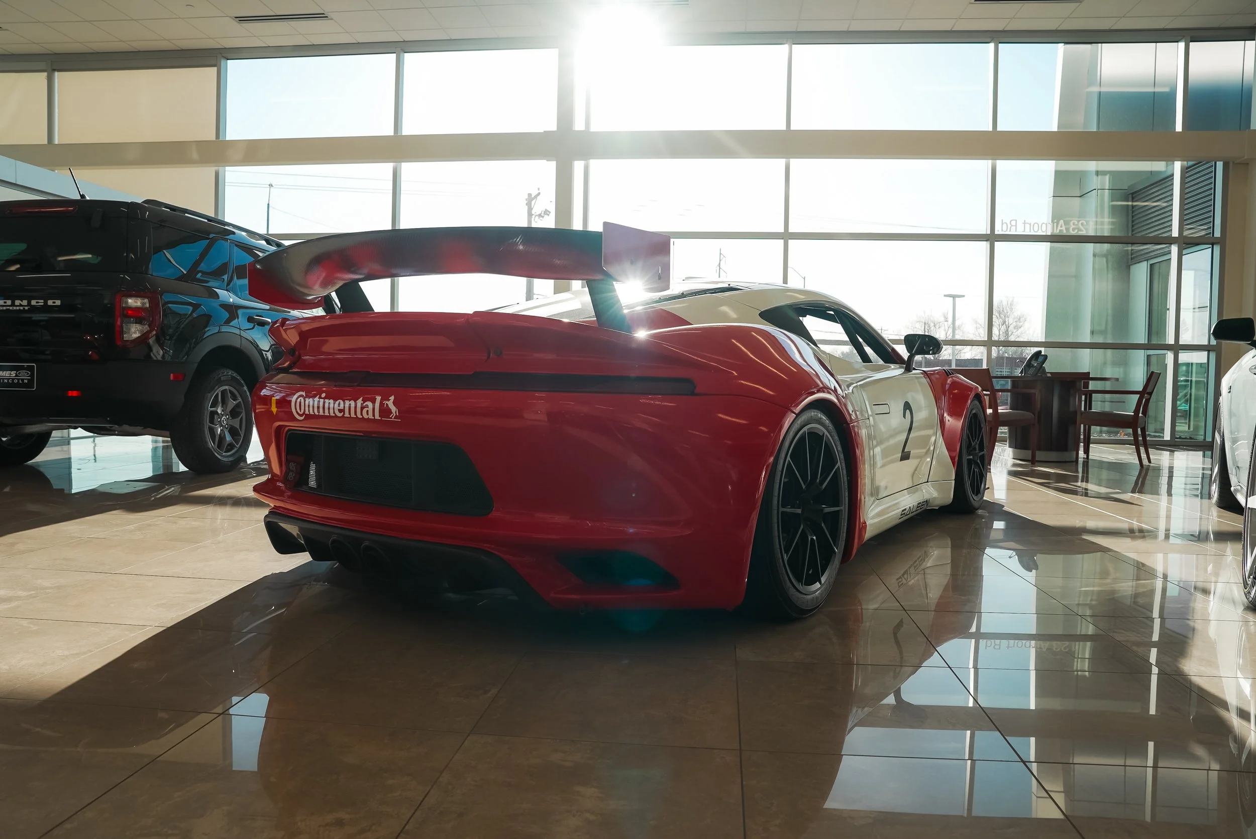 Red Saleen sports car with rear spoiler and Continental branding parked indoors next to a black SUV.