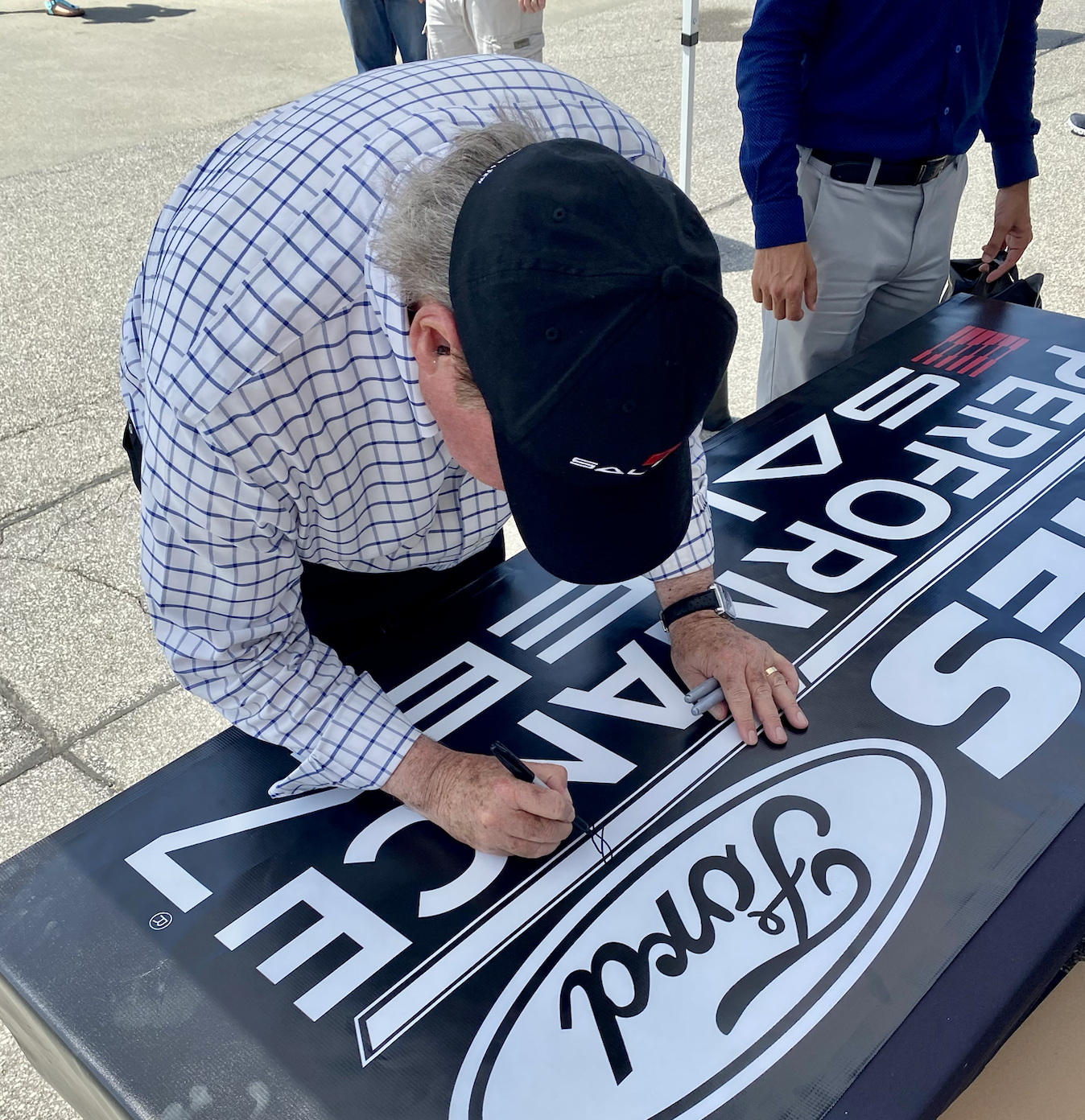 Steve Saleen signing a Ford performance banner outdoors