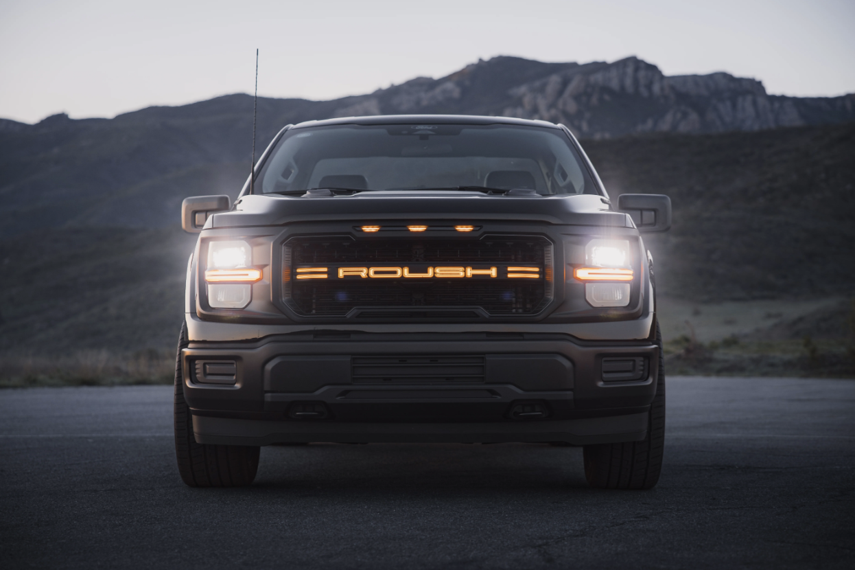 Close-up of a white Roush truck grille in a parking lot.