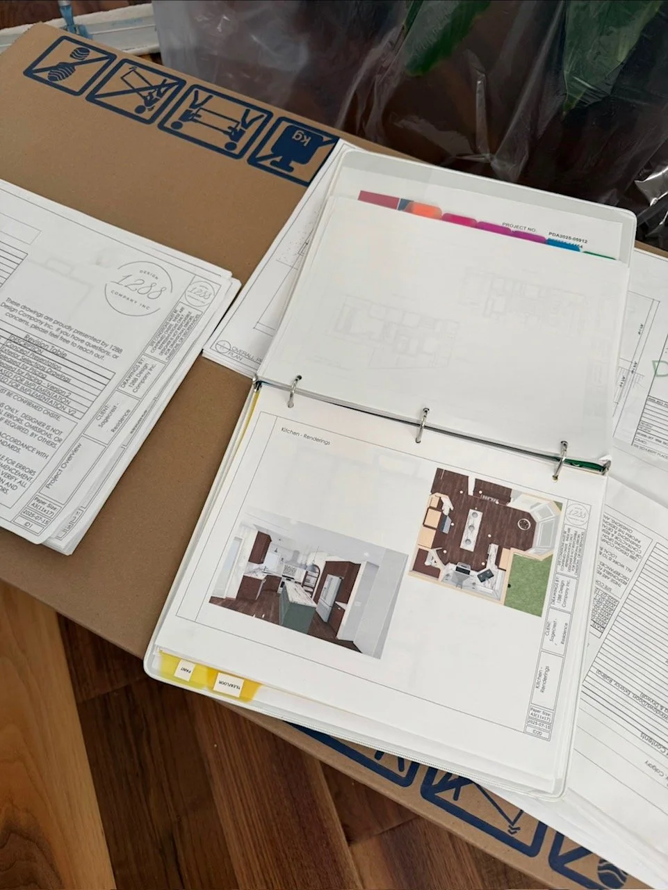 A desk with construction plans, printed architectural drawings, and photo renderings of a kitchen renovation project.