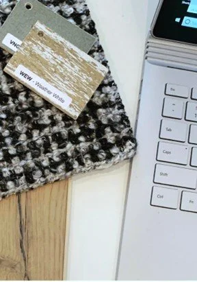 Close-up of a laptop keyboard, a small wooden and white card, and a textured gray and black surface on a wooden table.