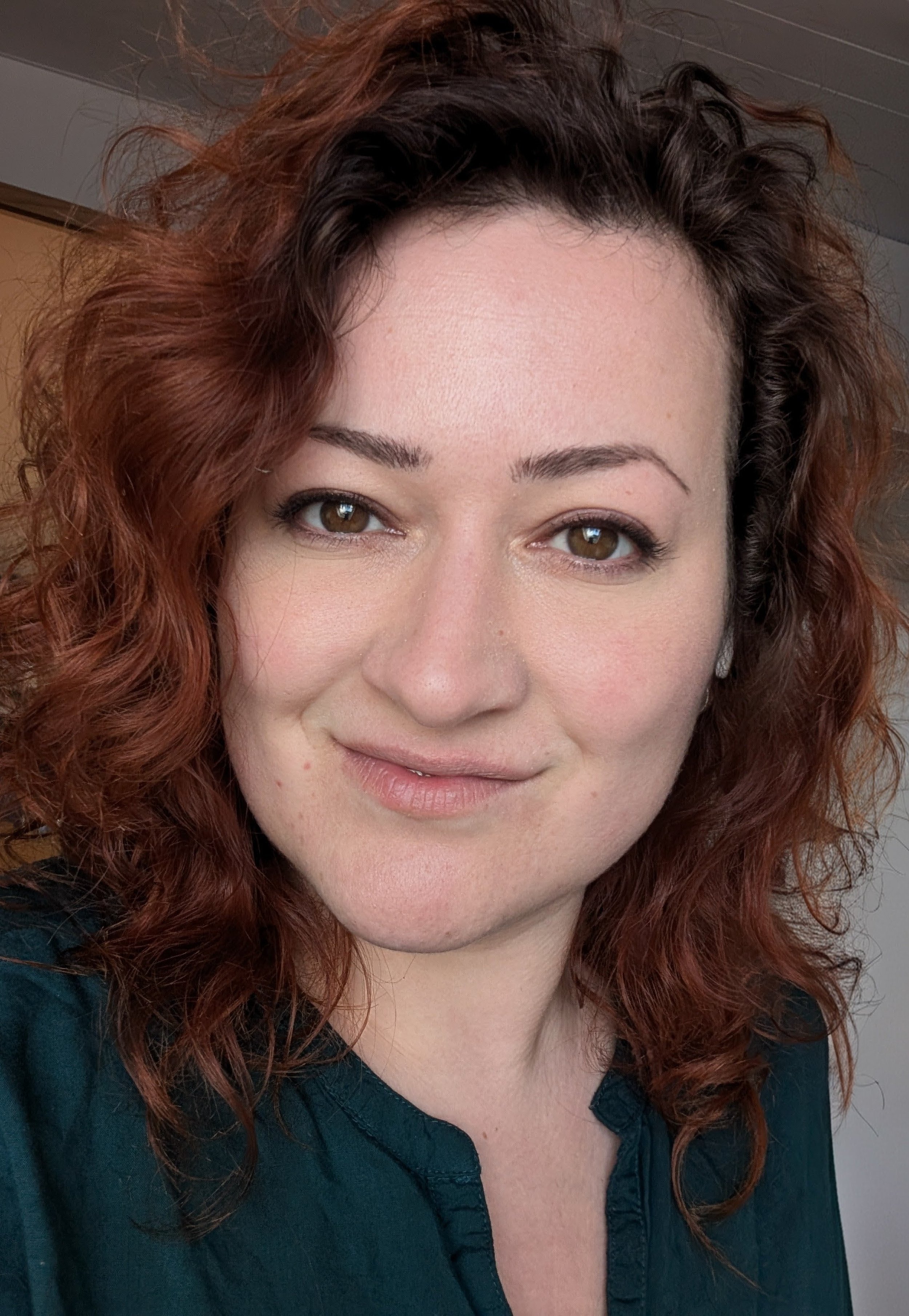 Nahaufnahme eines lachenden Mädchen mit braunen Augen, roten lockigen Haaren und dunklem Hemd.