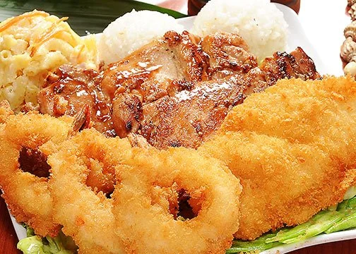 Fried calamari rings, grilled chicken, mashed potatoes with gravy, and fried fish fillet served with cauliflower rice and garnished with lettuce on a white plate.