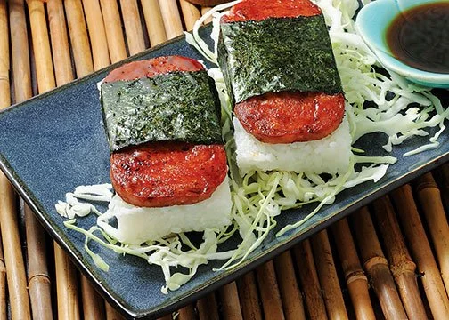 Two pieces of sushi topped with spicy tuna, seaweed, on shredded cabbage with soy sauce on the side