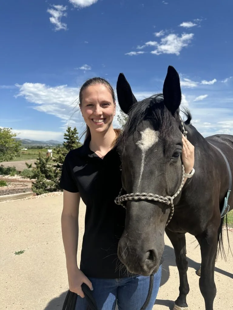 A woman smiling next to a black horse with a white star on its forehead.