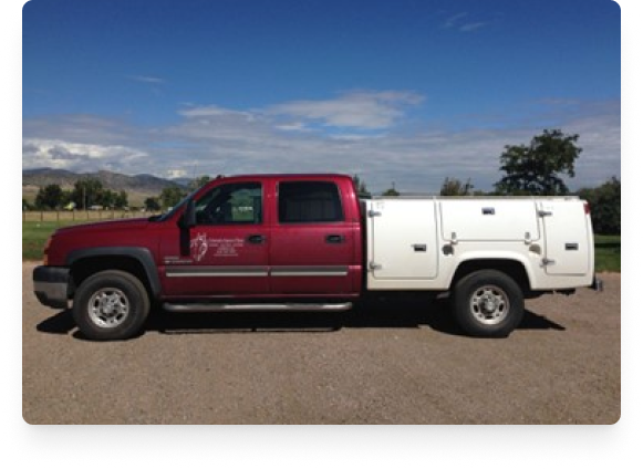 Red and white utility truck parked on a dirt area with trees and mountains in the background.
