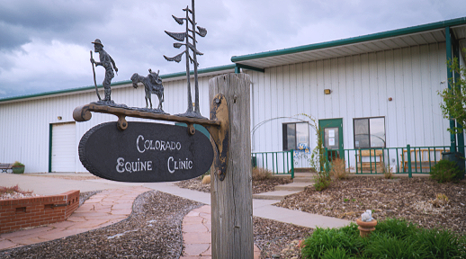 Sign for Colorado Equine Clinic featuring a cowboy, horse, and directional signs in front of a large white building.