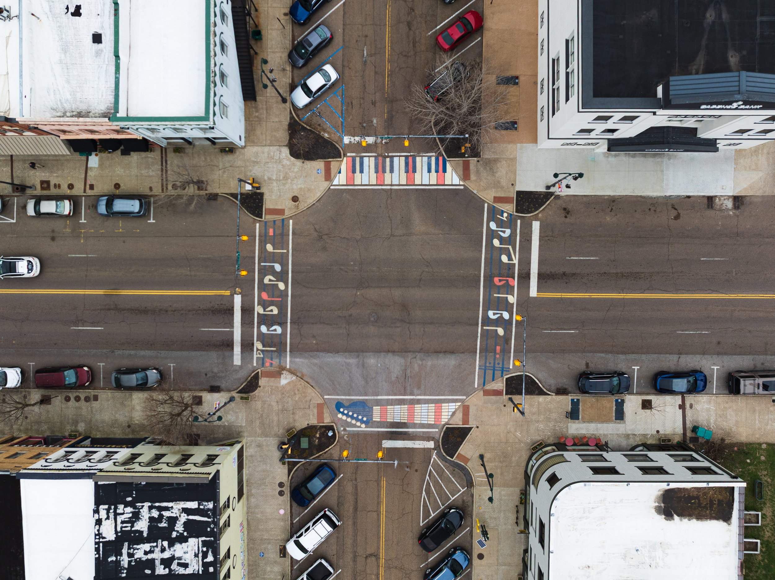 aerial view of crosswalk murals, painted with music notes, piano keys, and a guitar neck in shades of red, white, and blue