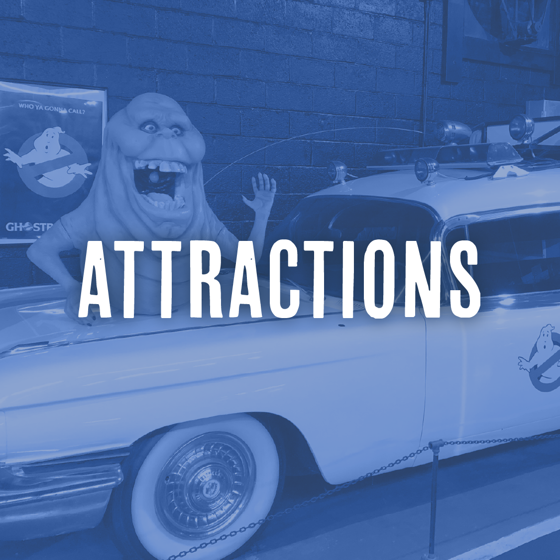 A vintage white car with a figure of Slimer from Ghostbusters standing on top, waving. There is a Ghostbusters logo poster on the brick wall behind the car, and the word "Attractions" is overlaid on the image.