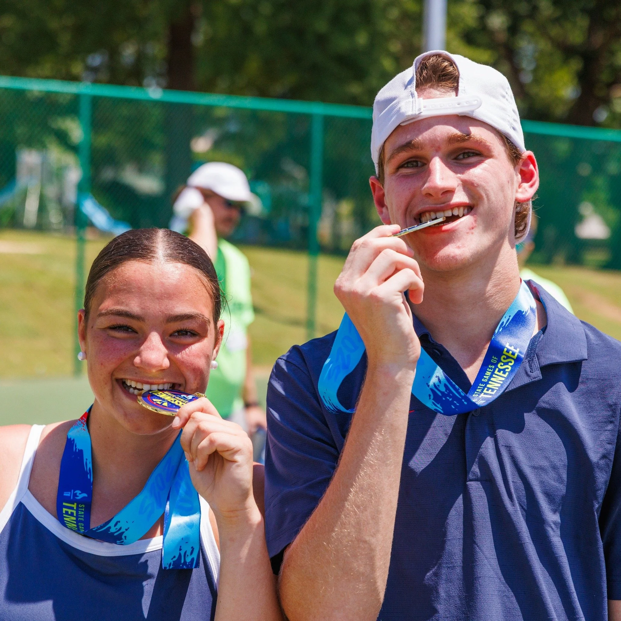 Happy young man and woman with medals around their necks, biting them, celebrating their State Games pickleball win
