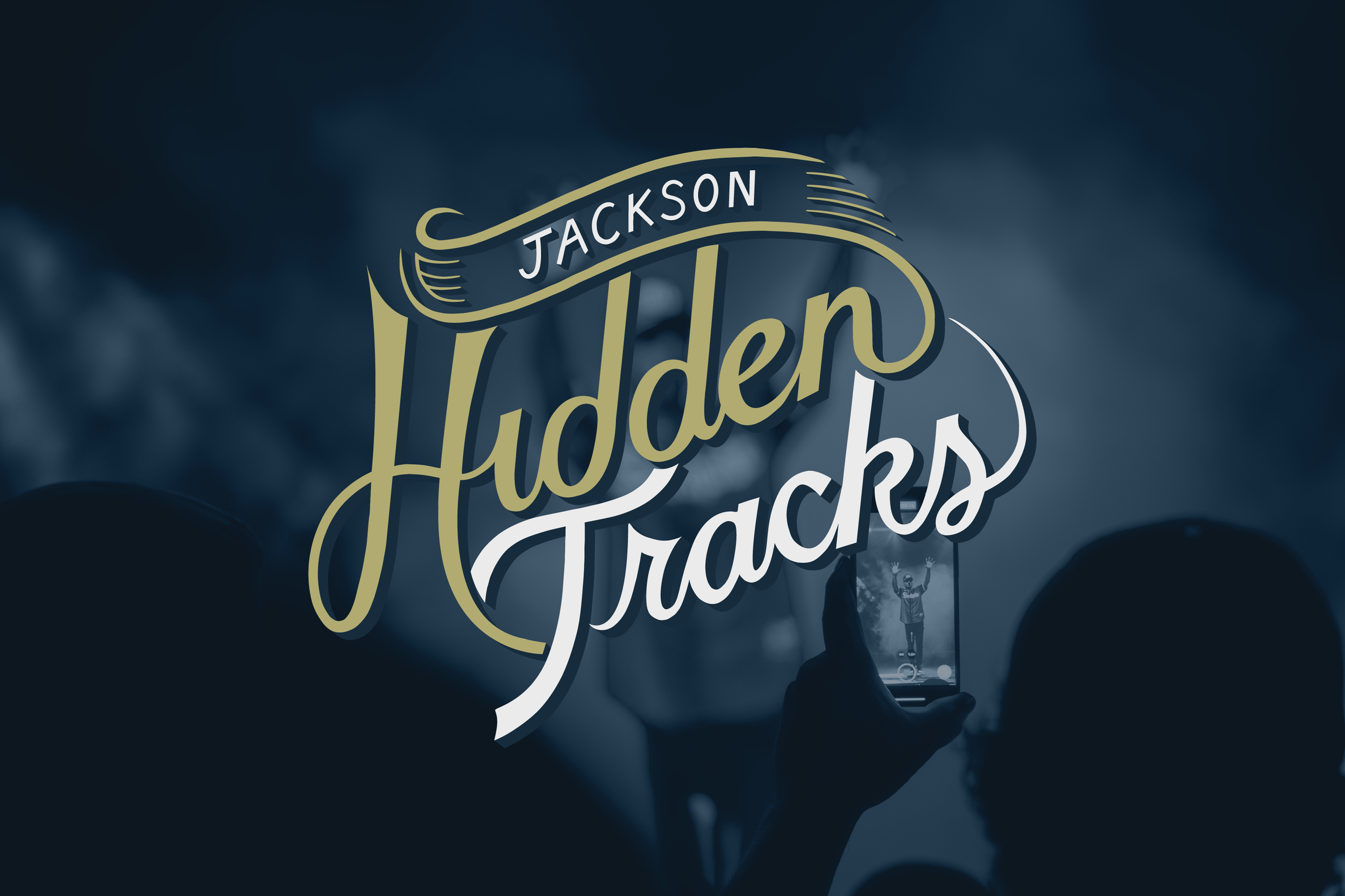 Photo of a person holding a smartphone at a concert with a logo on top for "Jackson Hidden Tracks"