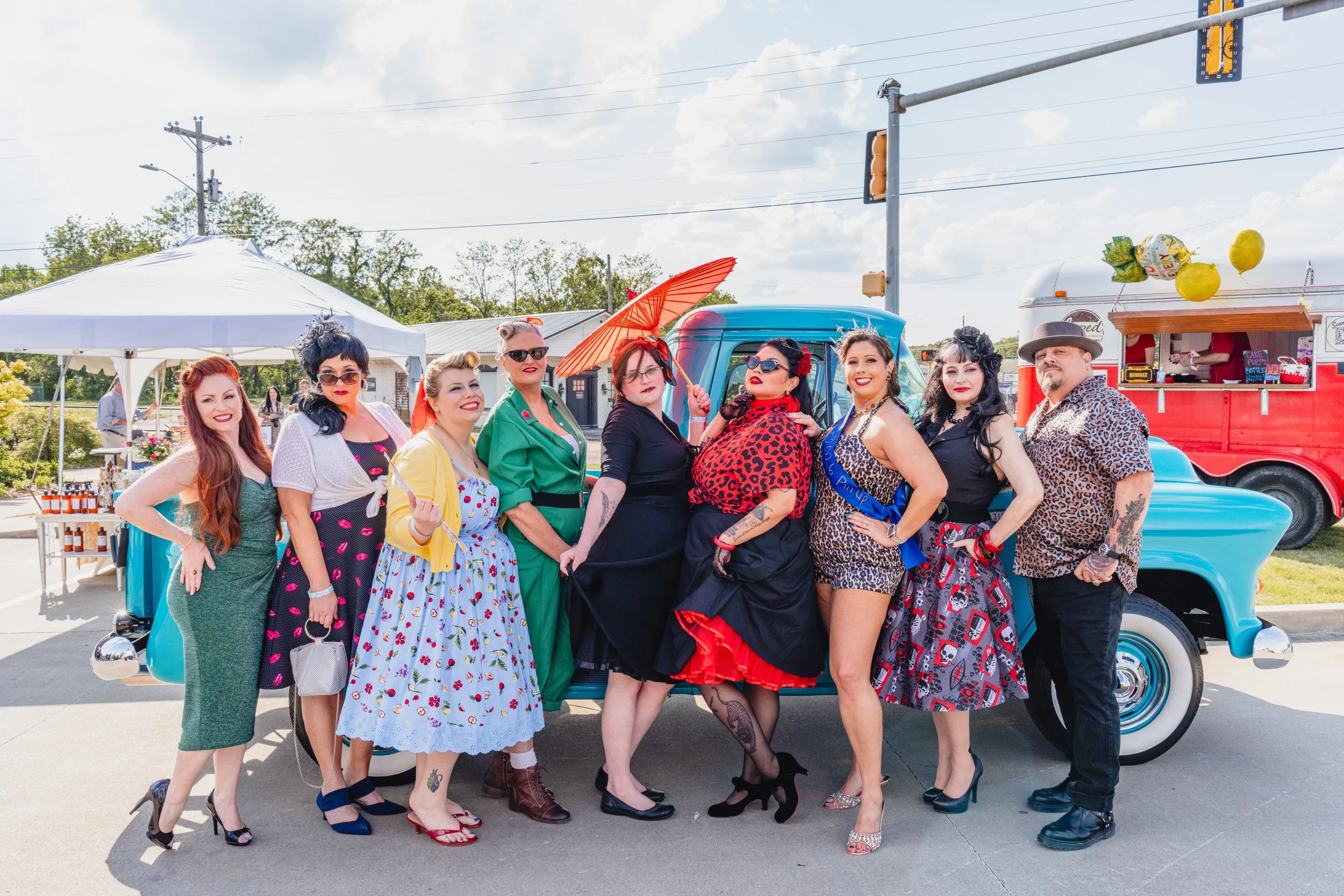 1950's pinup contestants smiling and posing for a photo in front of an old blue truck at the Blue Suede Rockabilly Weekend festival