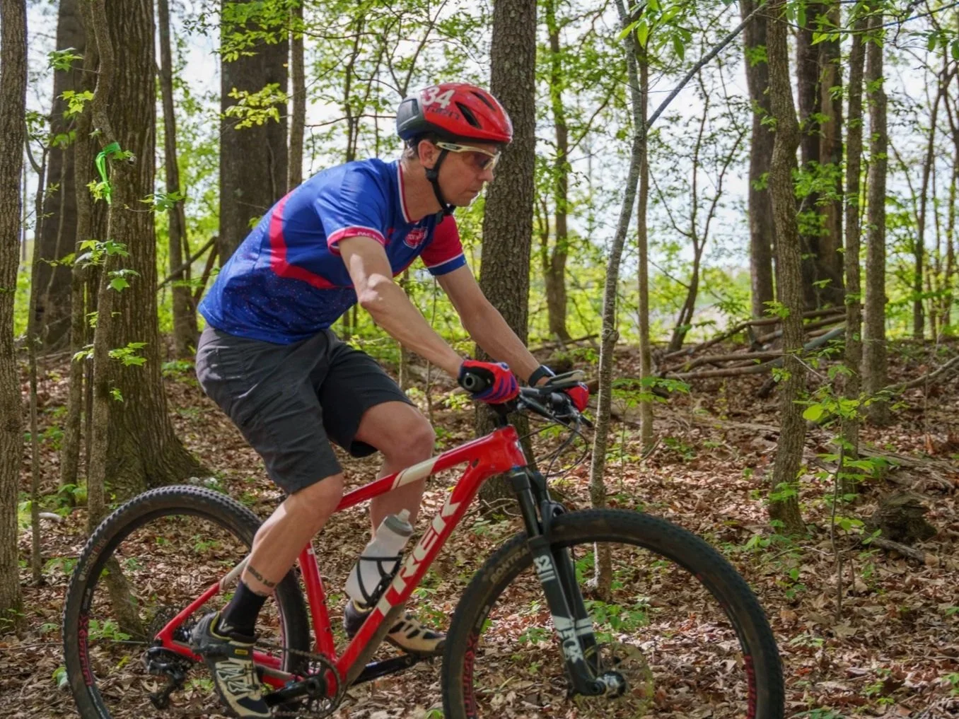 A man mountain biking on a trail in a forested area with trees and green foliage.