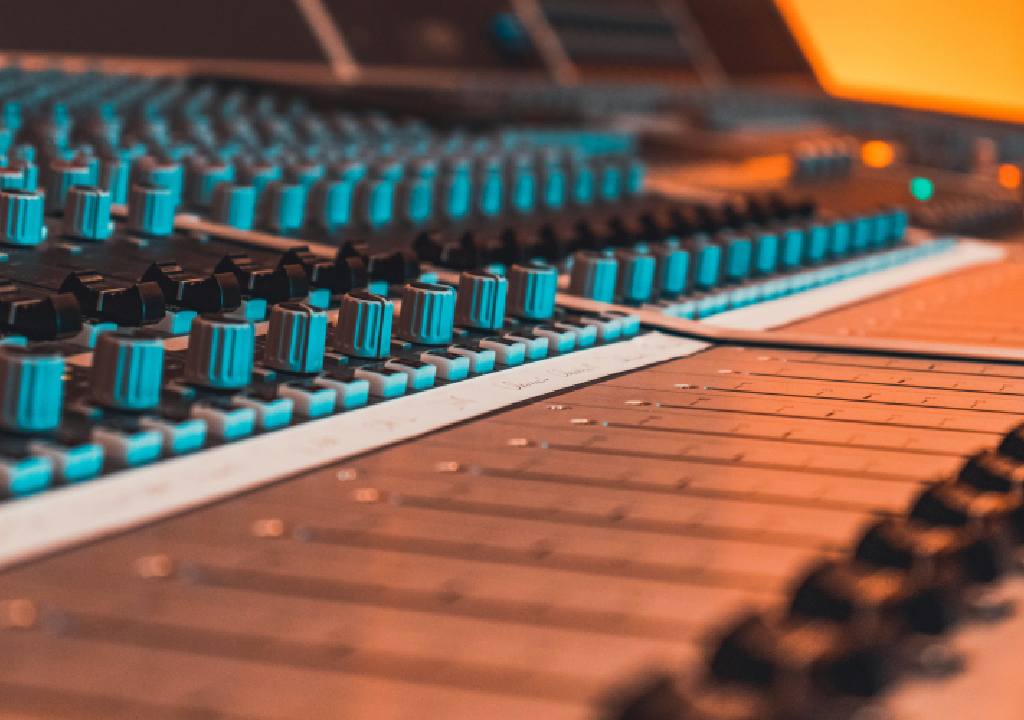Pannello di controllo audio con fader e manopole, luci blu e arancioni.