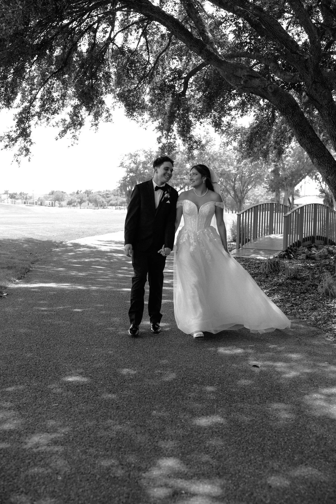 Bride and groom walking together beneath large shade trees at their Florida golf course wedding