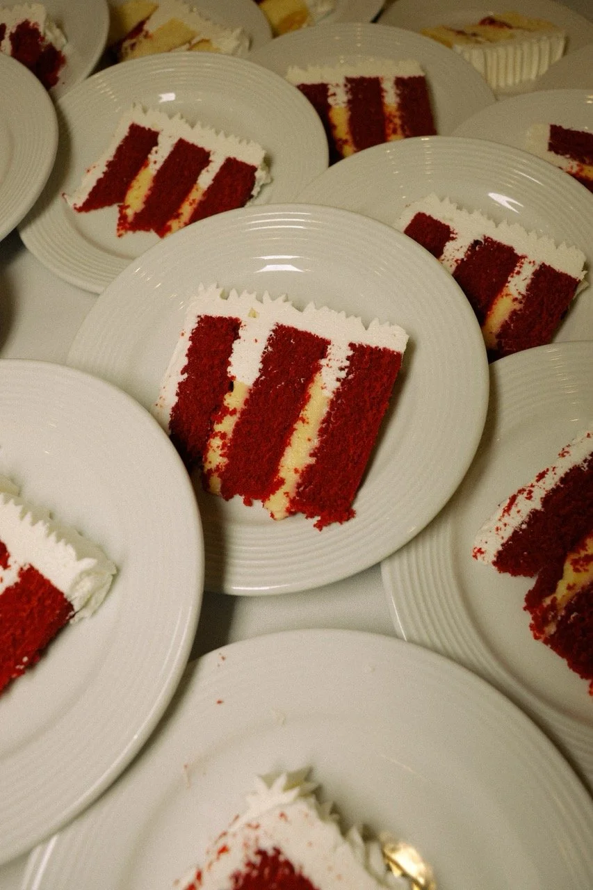 Slices of red velvet cake with cream cheese frosting on white plates at a wedding reception.
