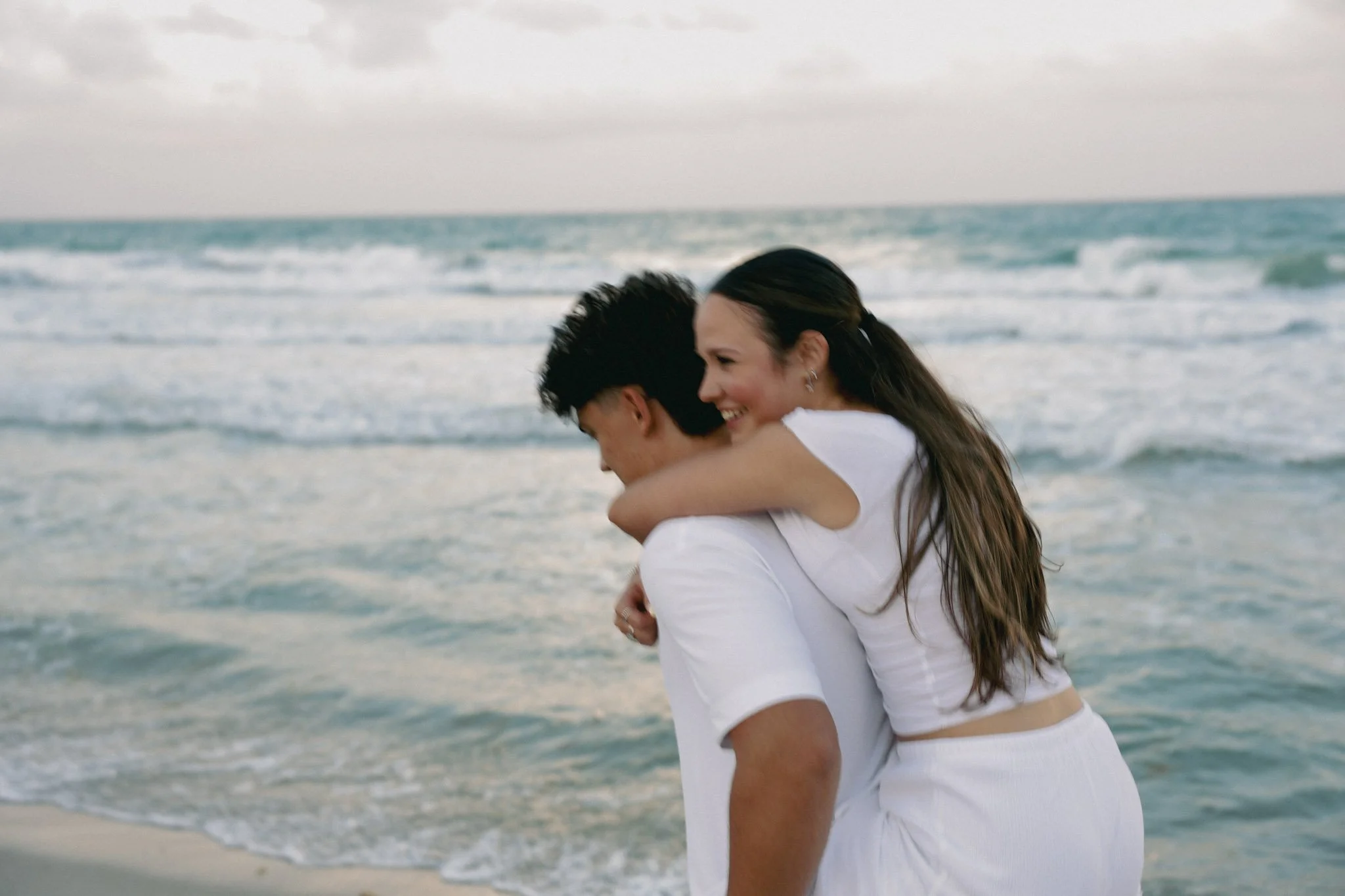 a couple embracing on a beach with the ocean in the background, the woman smiling and the man with his head down in Florida